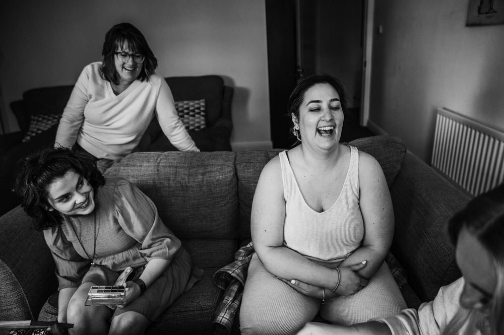 A candid black and white photograph showing people relaxing together on a couch in a casual indoor setting.