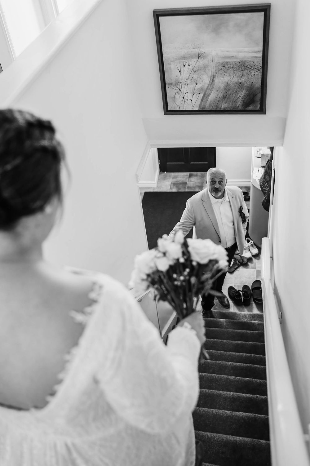 Black and white photo showing emotional first look moment on staircase as bride holds bouquet of flowers.