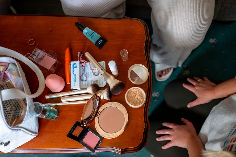 A collection of beauty and makeup products scattered on an orange surface including brushes and cosmetic containers.