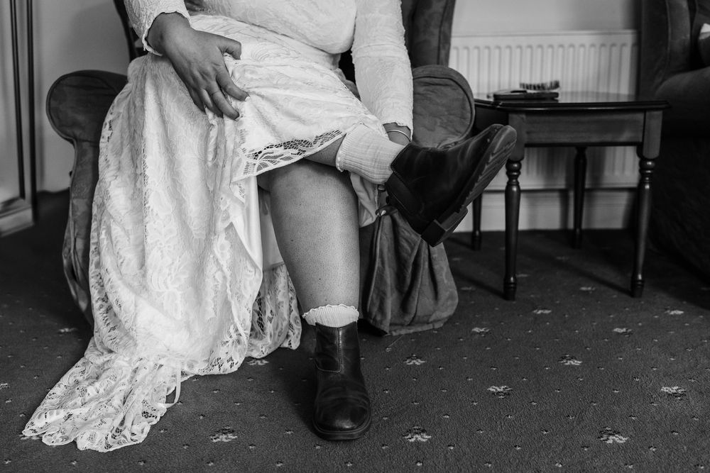 Black and white photo of boots being put on with a lace dress hem visible in an intimate indoor setting.