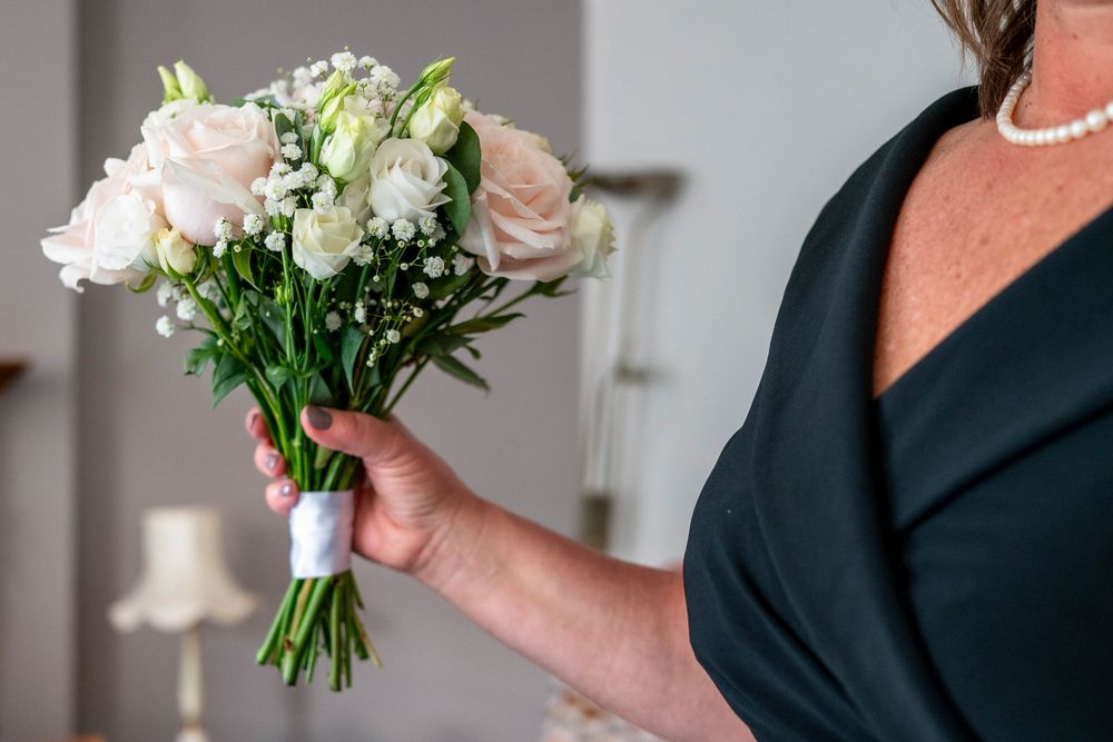 A hand holding an elegant bridal bouquet of pink roses and white flowers wrapped with a light ribbon.