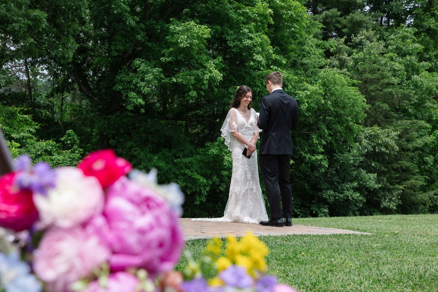 Couple shares intimate moment in lush green garden setting with vibrant pink and purple flowers in foreground. Tennessee Wedding.