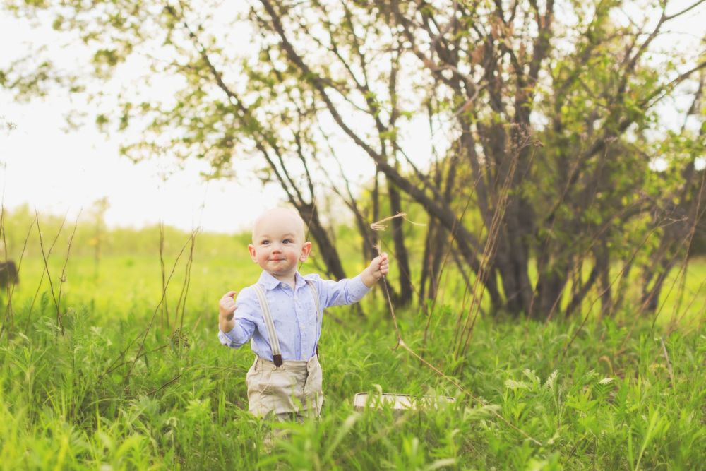 A child runs joyfully through a springtime meadow with tall grass and budding trees in the background.