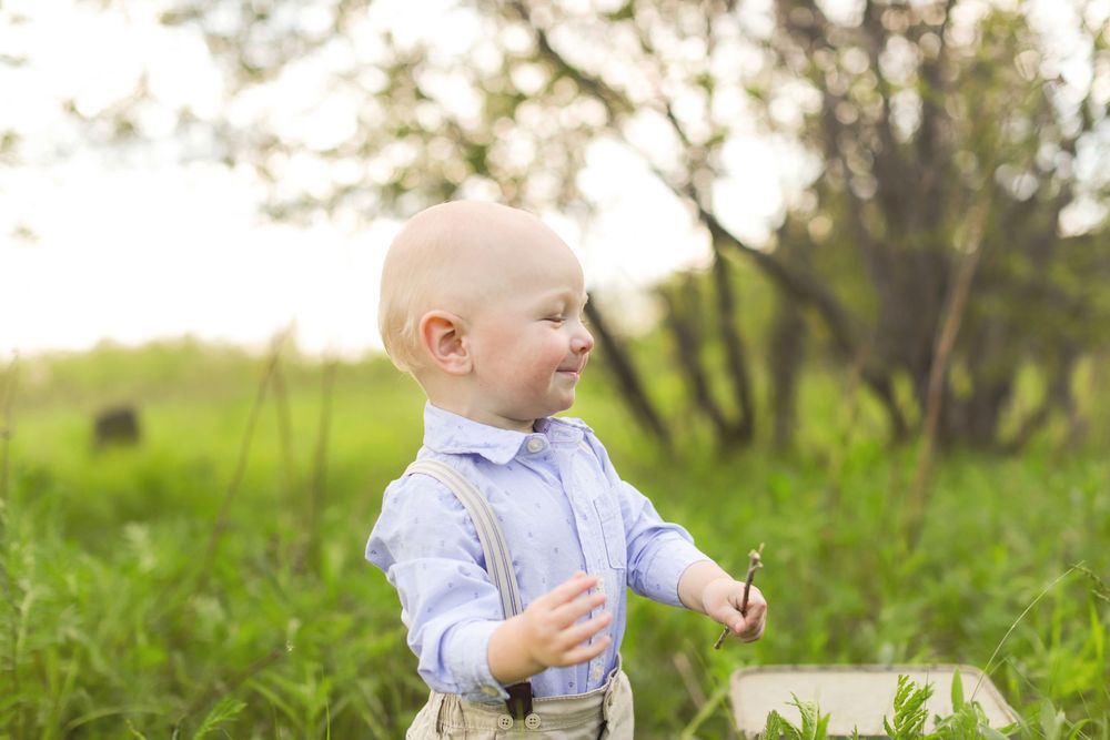 A joyful child wearing a light blue shirt plays in a green grassy field on a sunny day.