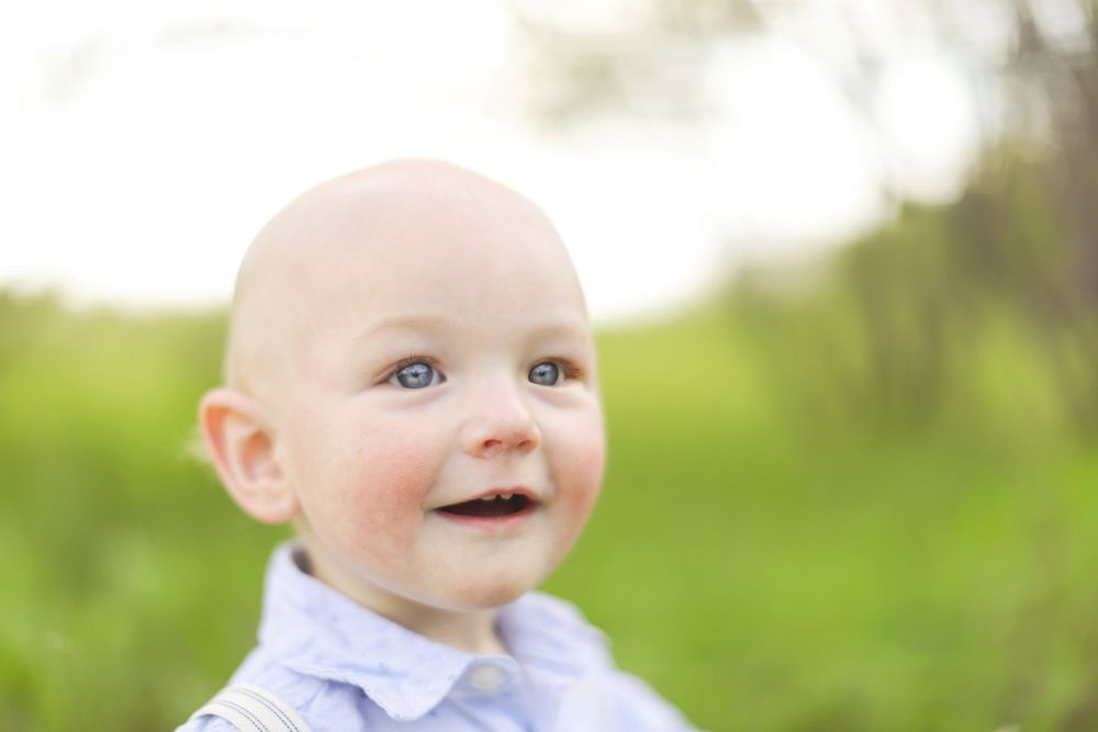 A young child smiling outdoors against a blurred green natural background in soft lighting.