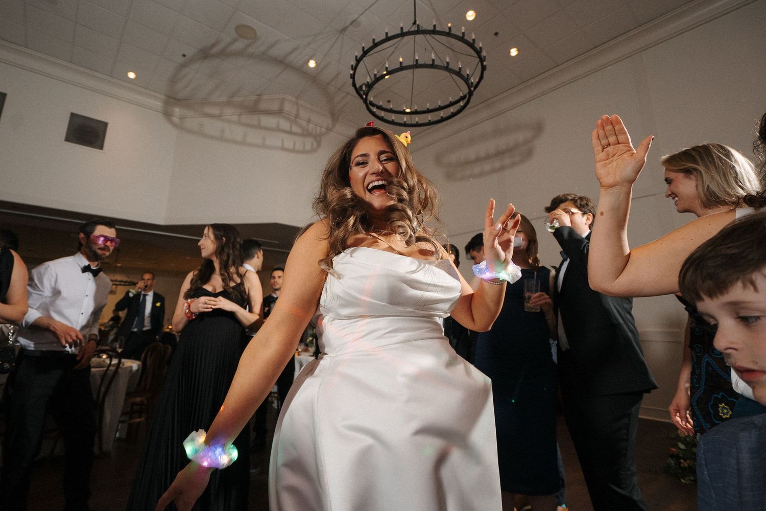Wedding guests dance together on the dance floor during an indoor wedding reception celebration.