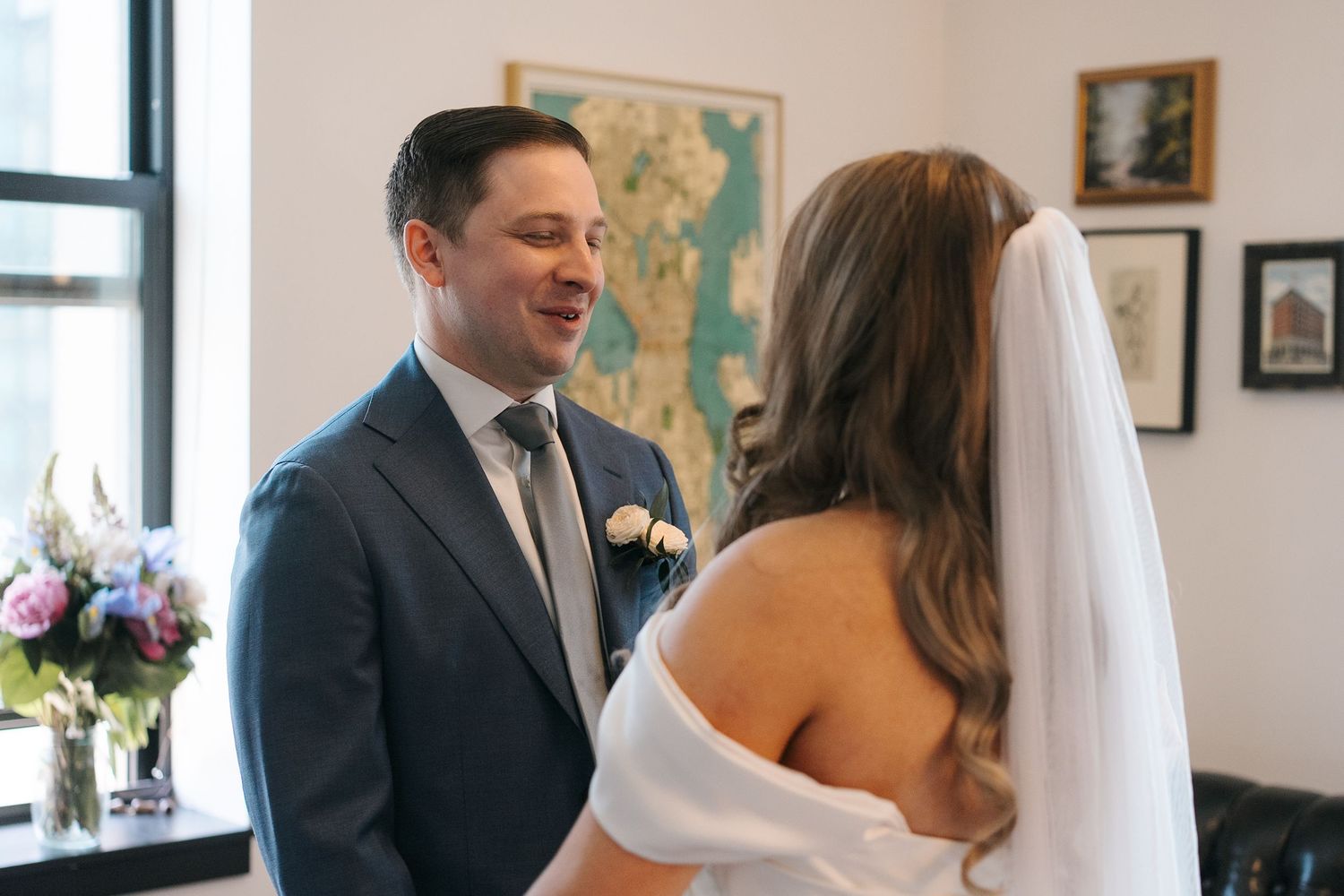 Wedding couple shares intimate conversation while photos are taken in an indoor venue with natural lighting.