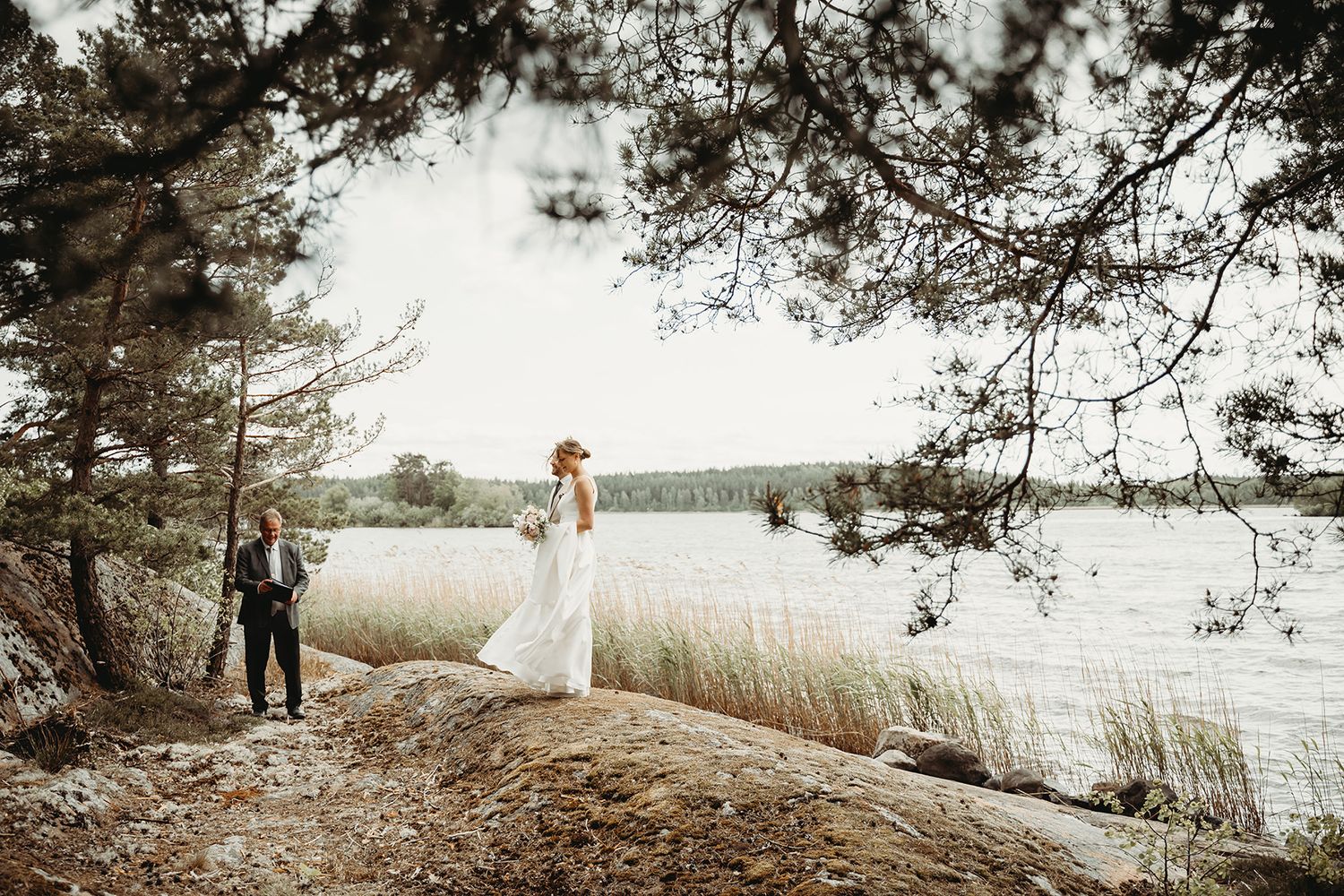 Vigselplats vid havet på en klippa i Södermanland, brudparet står vid vattnet med vigsel förrättaren intill. Intim vigsel utomhus i Nyköping