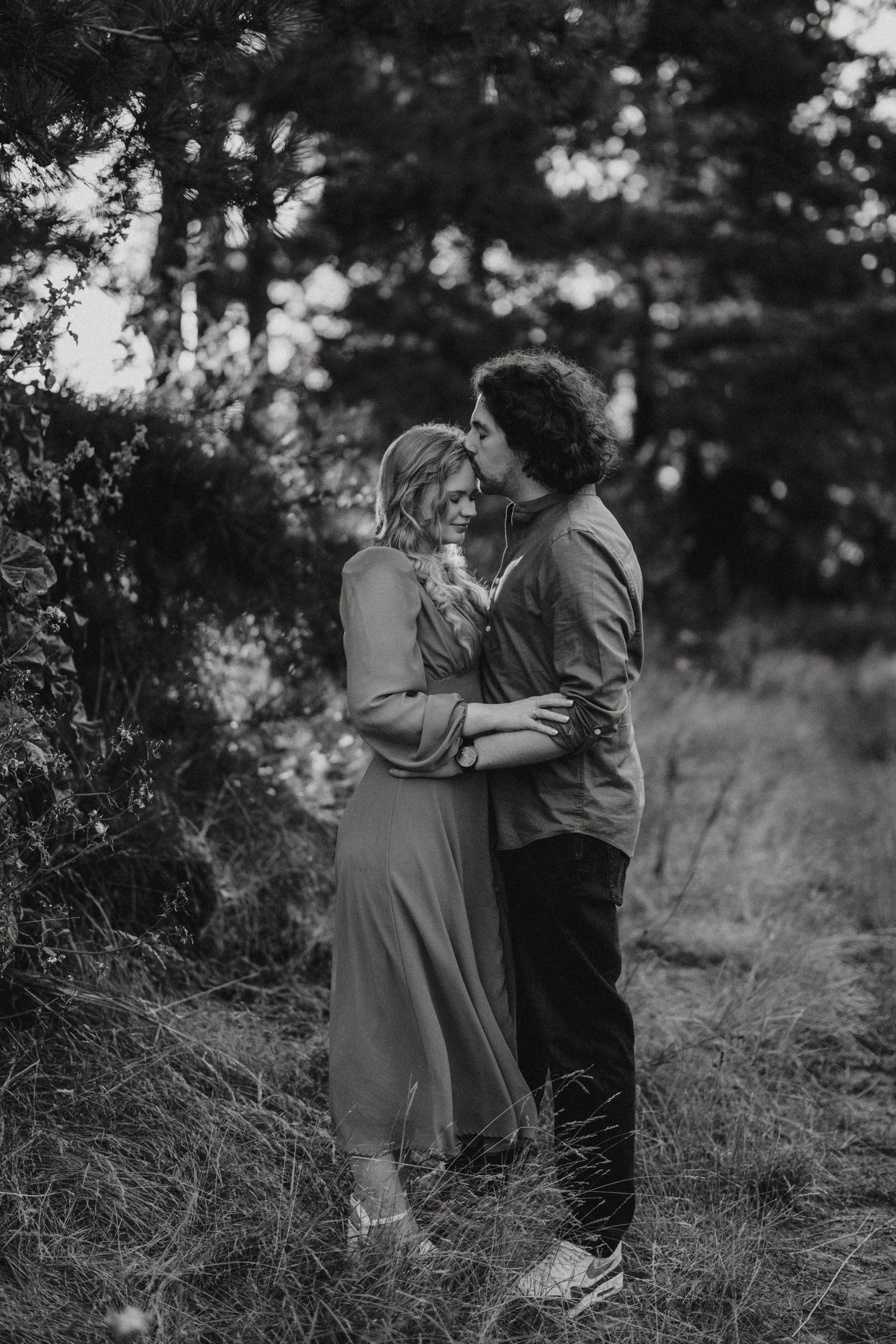 A romantic black and white photograph of a couple embracing on a nature trail surrounded by dreamy lighting. By Lincolnshire photographers.