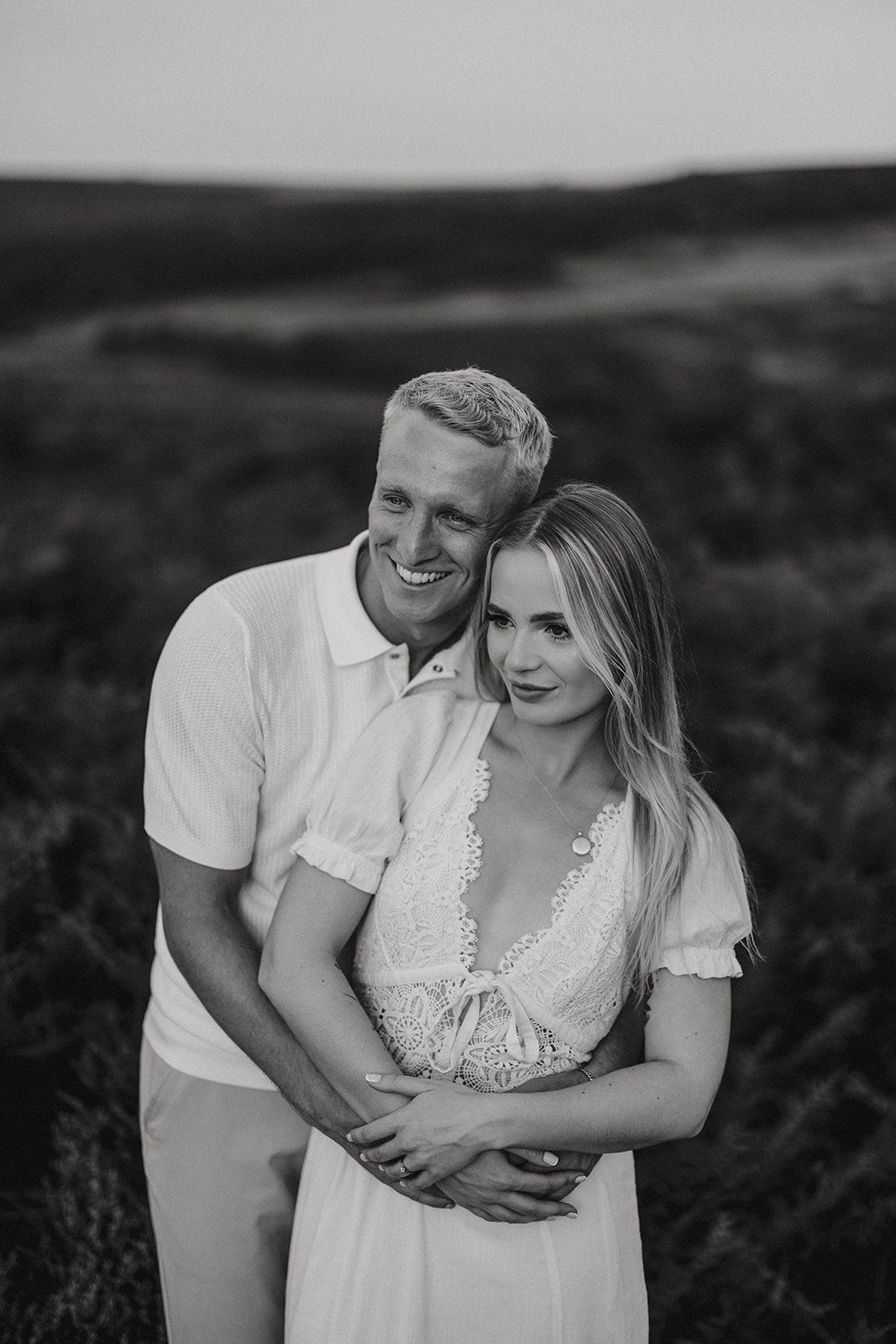 Black and white romantic photo of a couple in white outfits embracing in a field at sunset. Captured by Lincolnshire photographers.