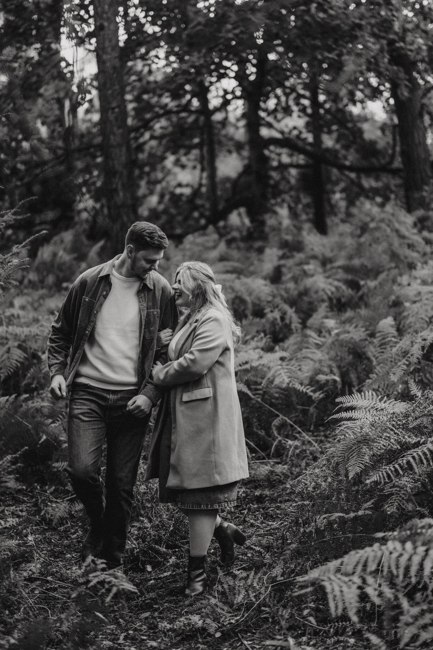 A couple takes a romantic stroll through a misty forest path surrounded by lush ferns in black and white. Taken by Lincolnshire photograpers
