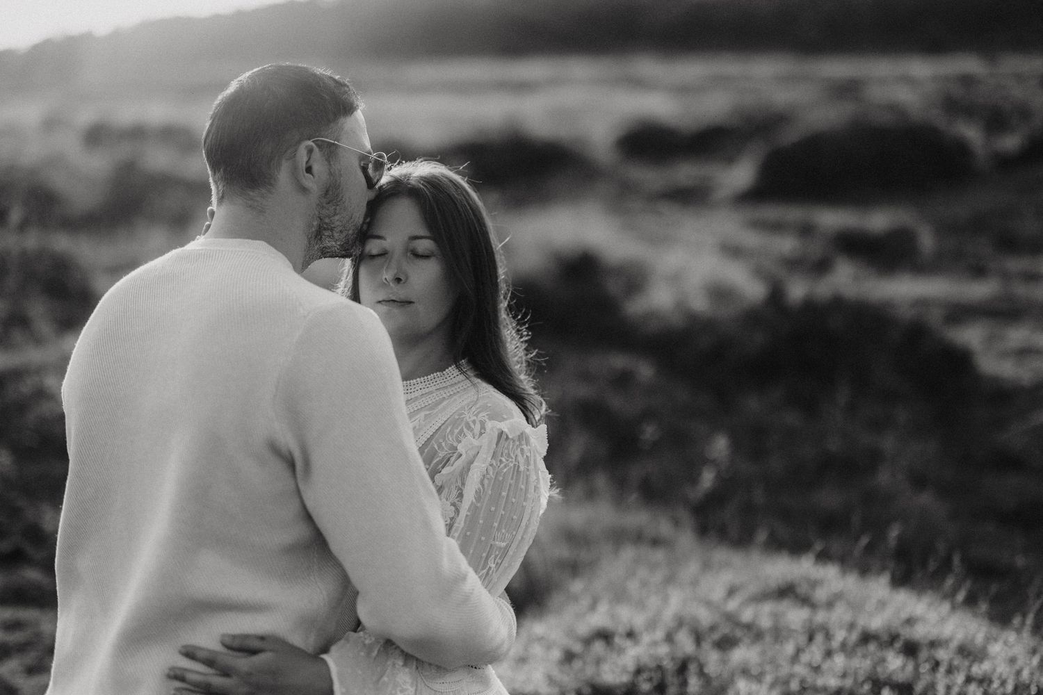 Couple embraces in romantic black and white outdoor portrait against rolling hills landscape. Captured by Lincolnshire photographers.