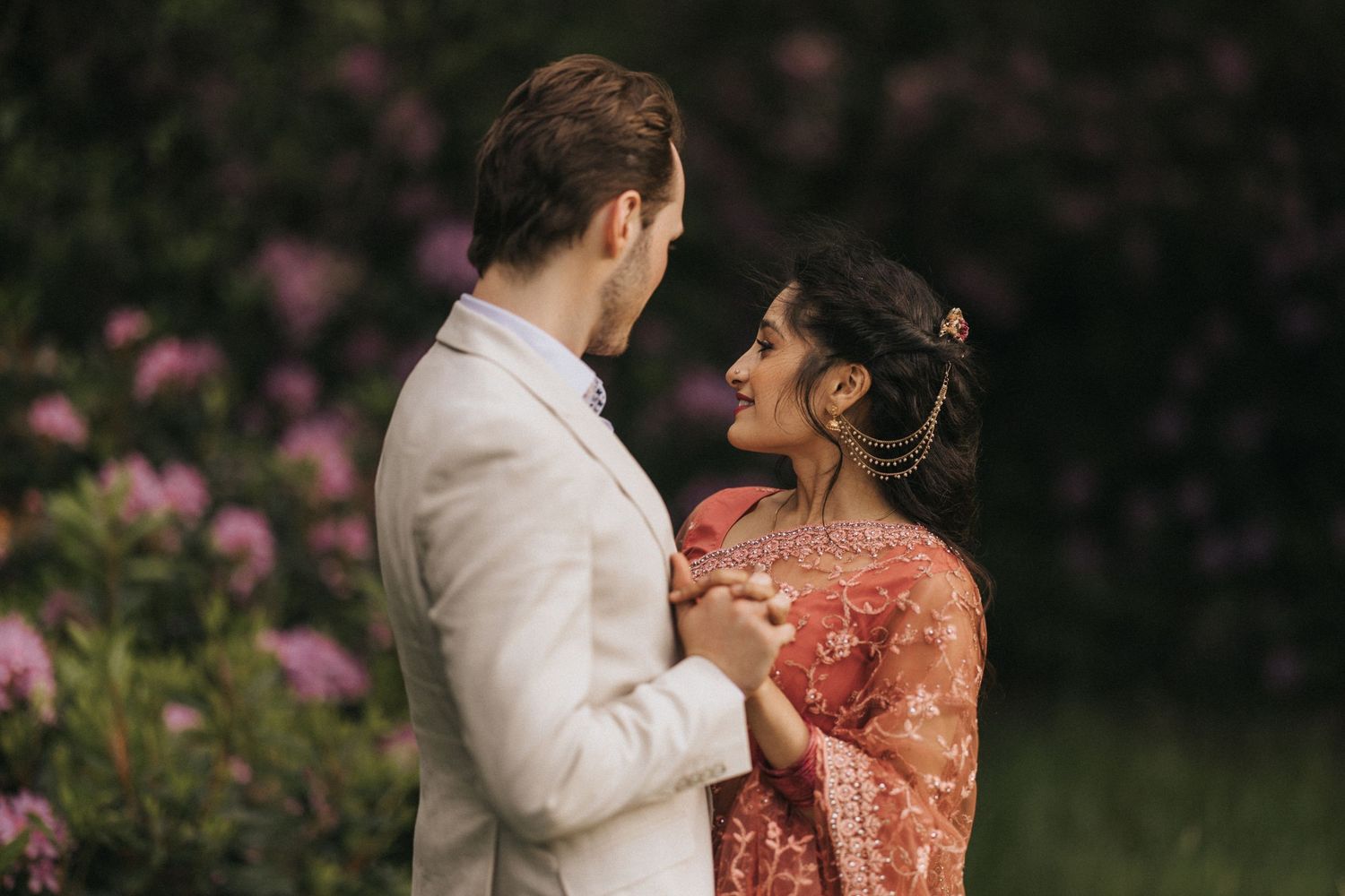A newly engaged couple share an intimate moment together in a garden with pink flowers. Captured by Lincolnshire photographers.