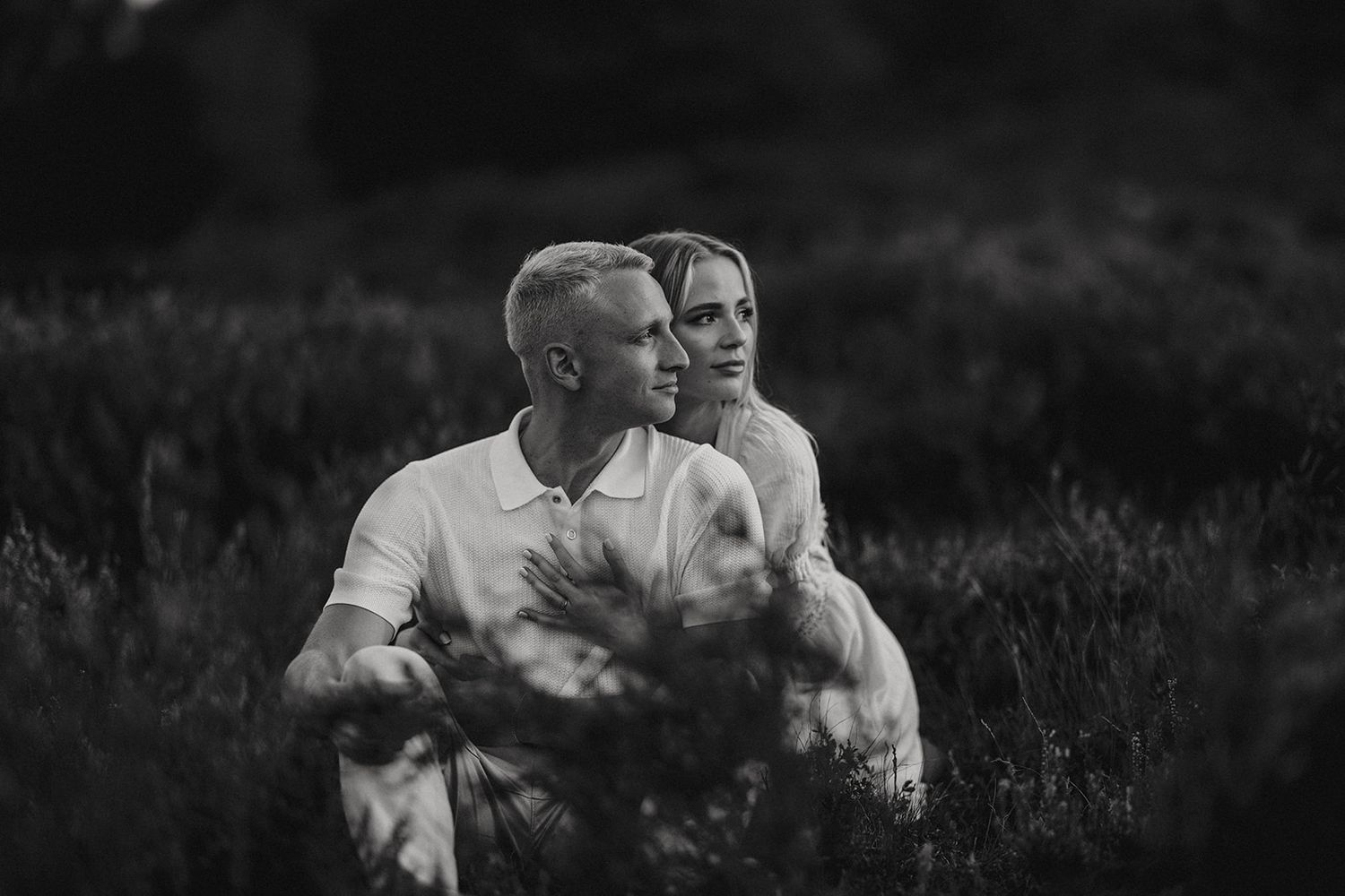 A couple embraces tenderly in a field at dusk, creating an intimate black and white moment. Captured by Lincolnshire photographers.