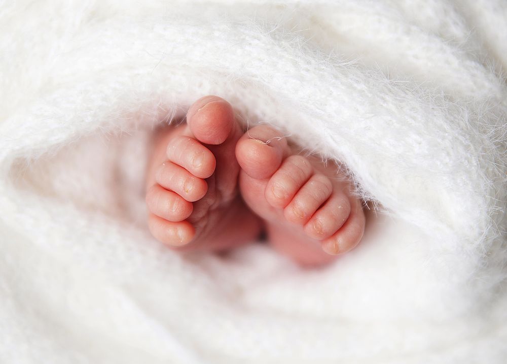 Tiny baby feet peek out from underneath a soft white blanket in a tender newborn photograph.