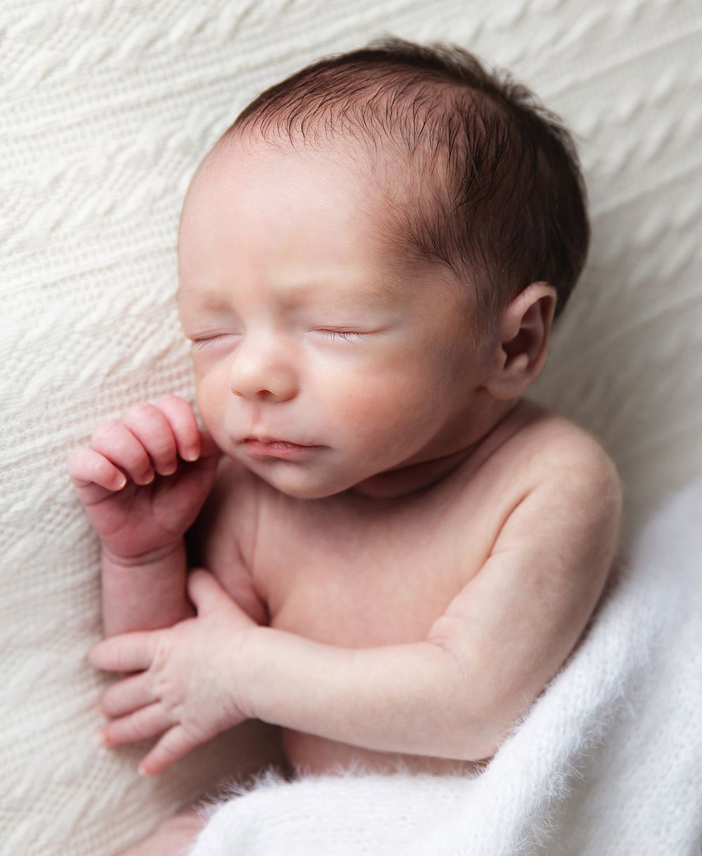 Peaceful sleeping newborn baby with closed eyes lying on white blanket, hand curled near face.
