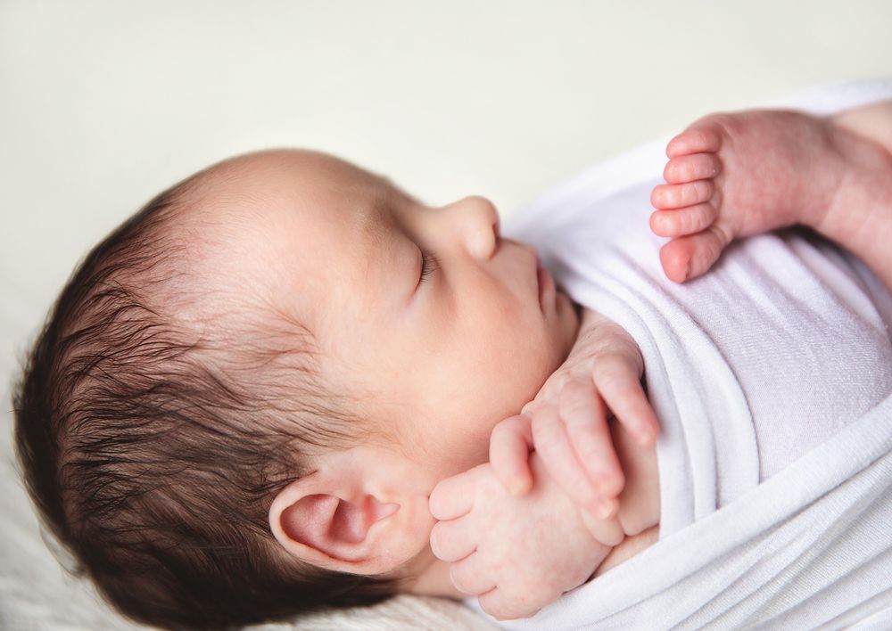 A sleeping baby in white clothing lies peacefully with a small curled foot visible.