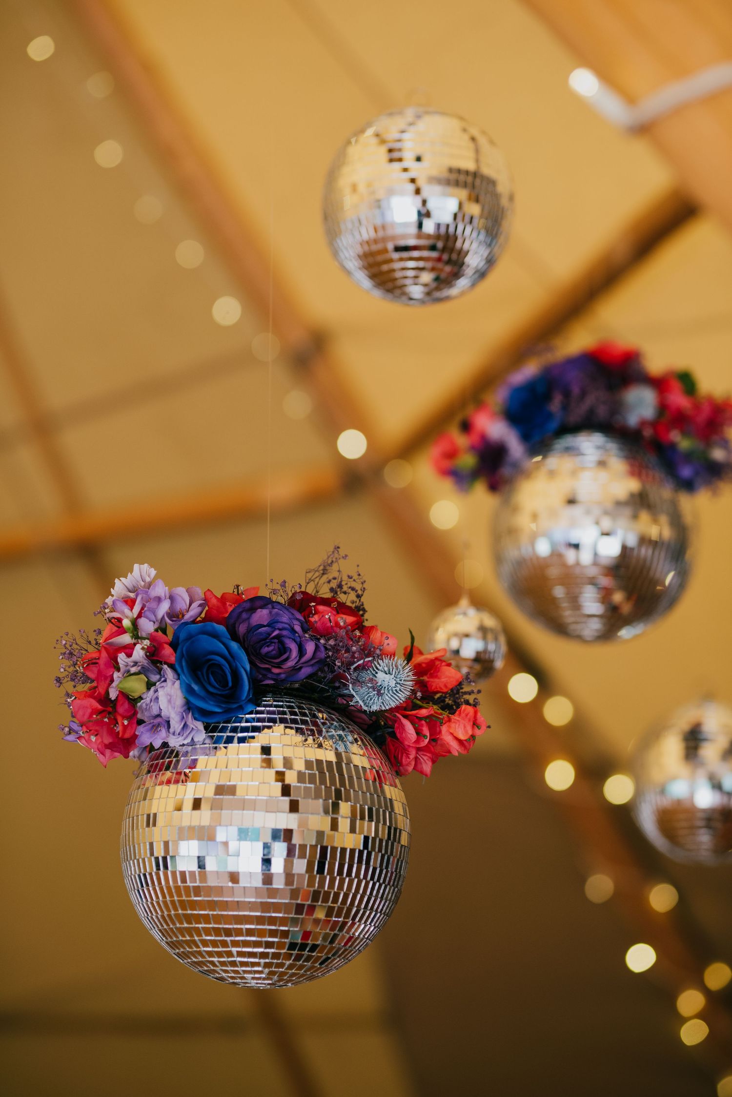Disco balls decorated with blue and pink flowers hang from ceiling with glowing string lights in background.