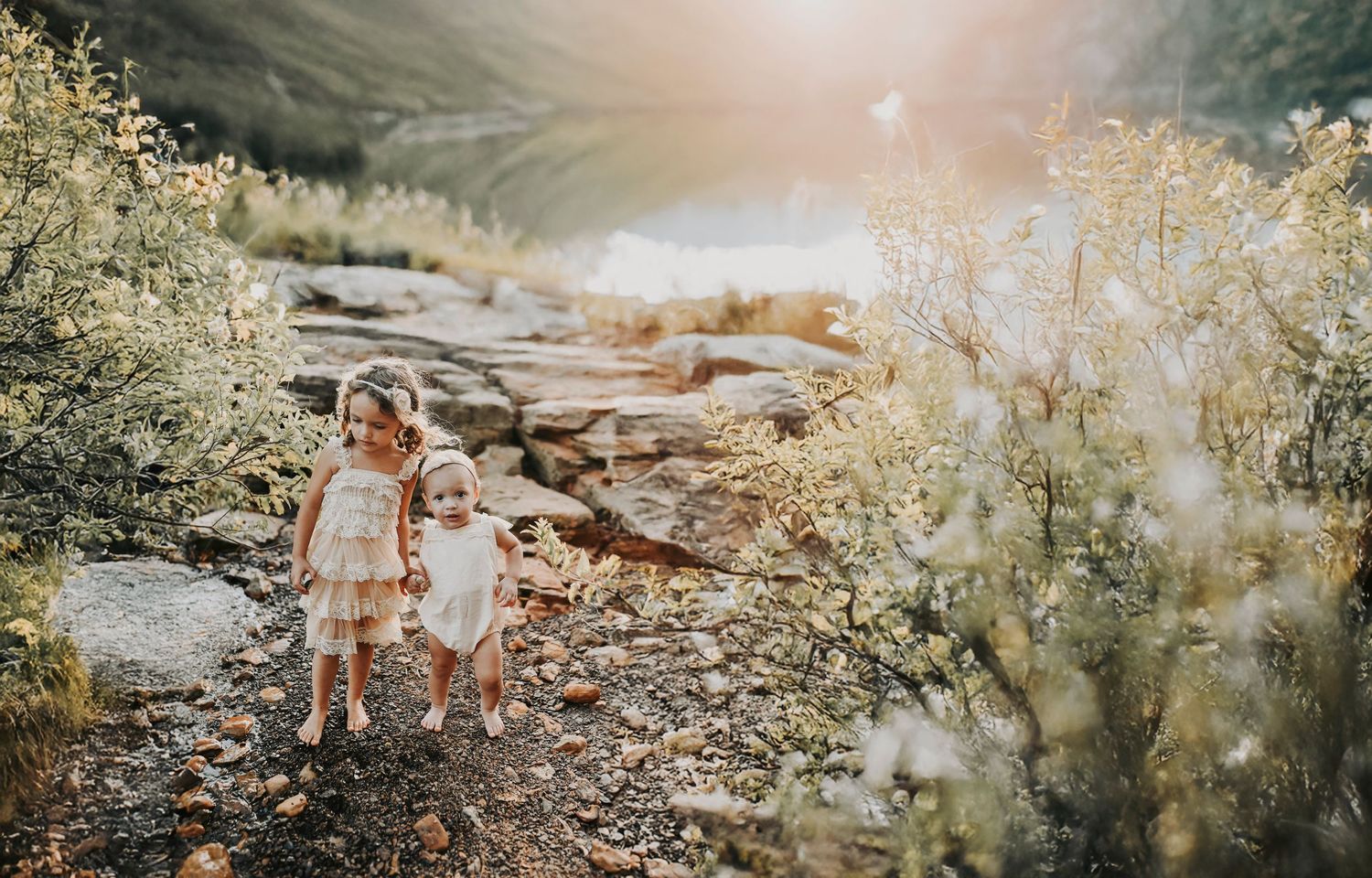 two little sisters hold hands and walk along a beach at sunset