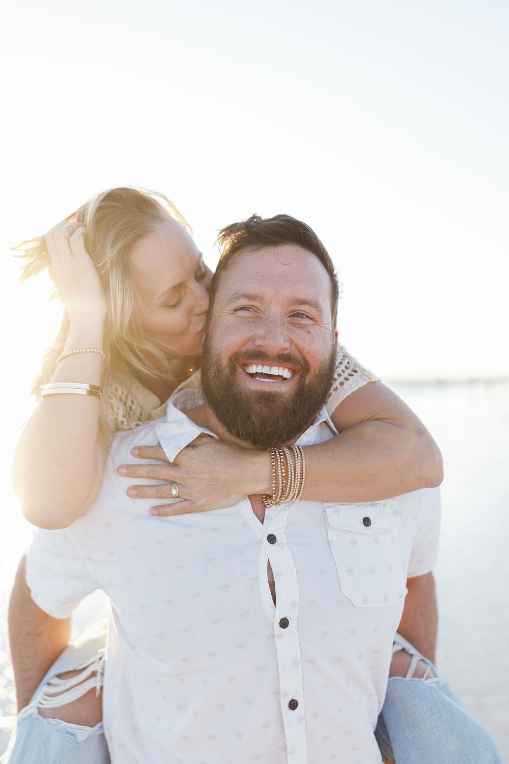 Piggyback ride on the sand with bright sunlight behind them