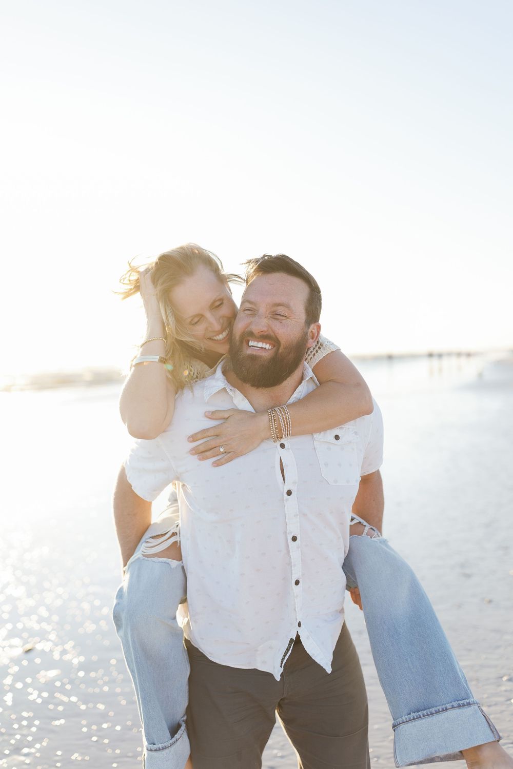 Backlit beach portrait of the engaged couple walking toward the waves