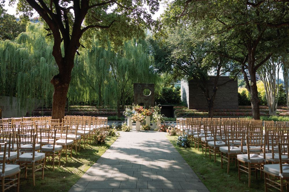 Outdoor garden wedding ceremony setup with wooden chairs and willow trees creating a romantic natural backdrop.