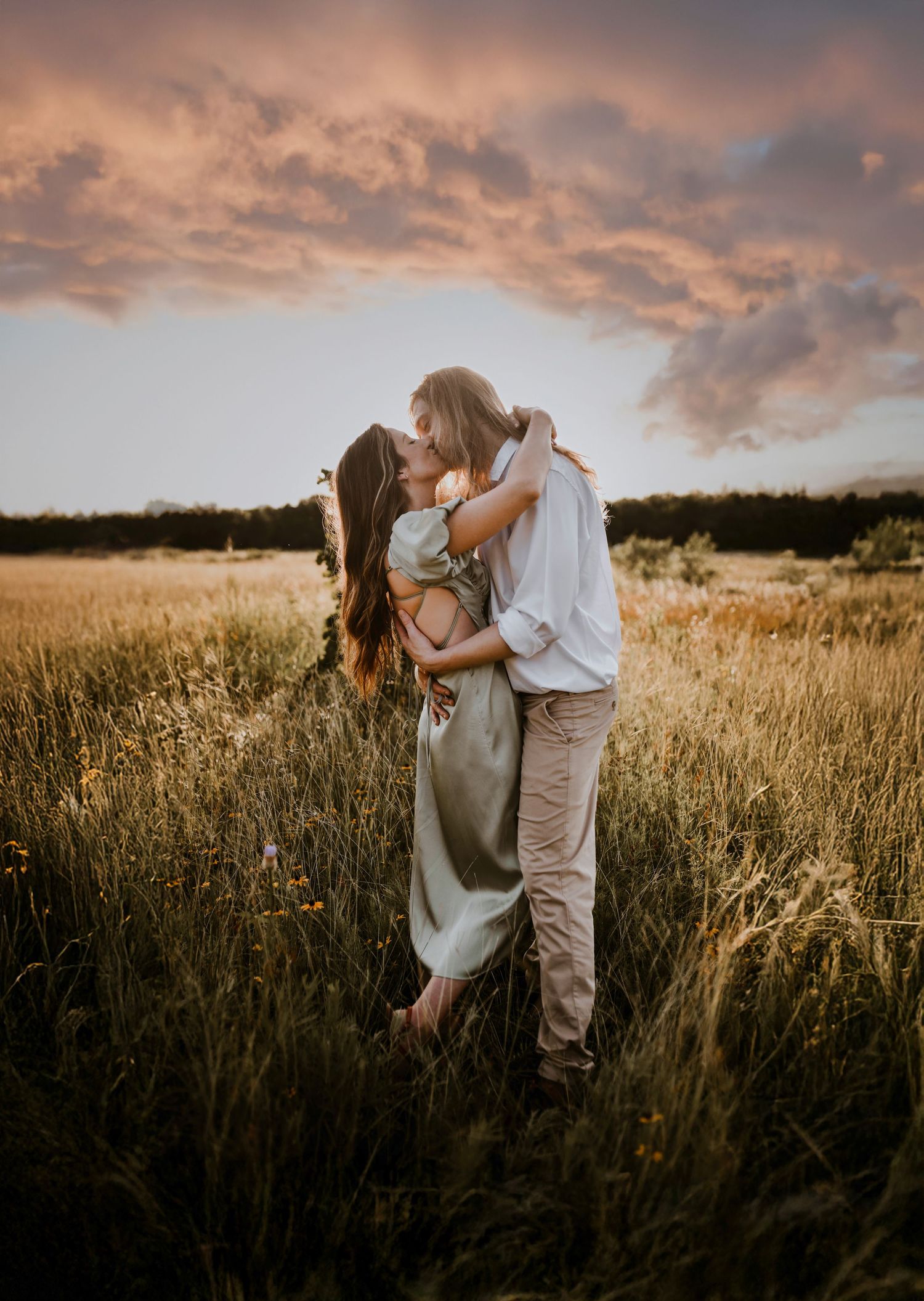 Sunset flares behind couple hugging in a field of dried grass