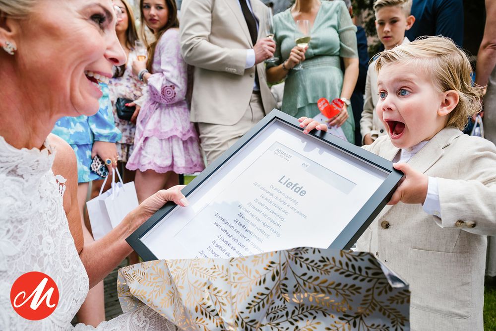 A person in a white wedding dress shares an exciting moment with a small child while showing a framed document.