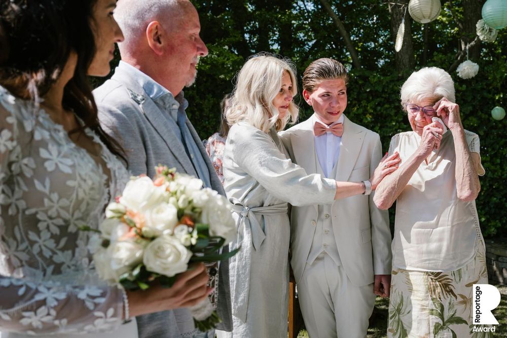 Guests gather outdoors at an elegant wedding celebration in a lush garden setting with white floral arrangements.