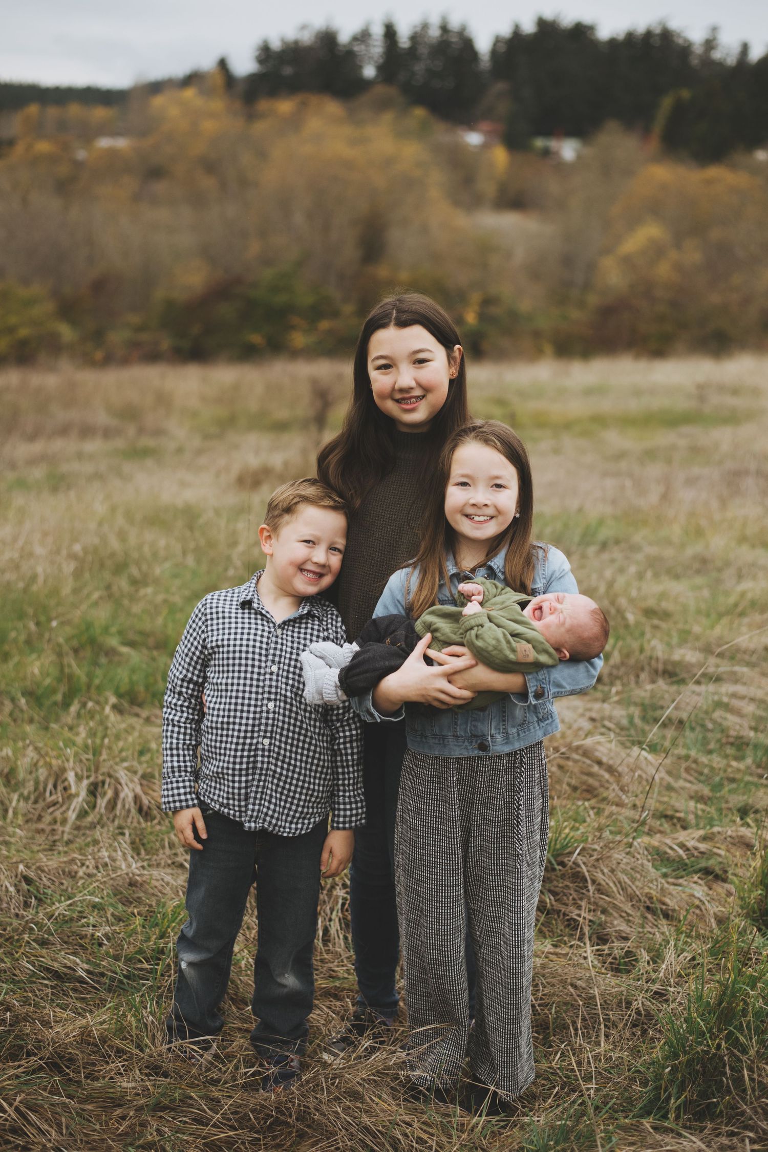 A family poses together in a grassy field on an autumn day with trees in the background.