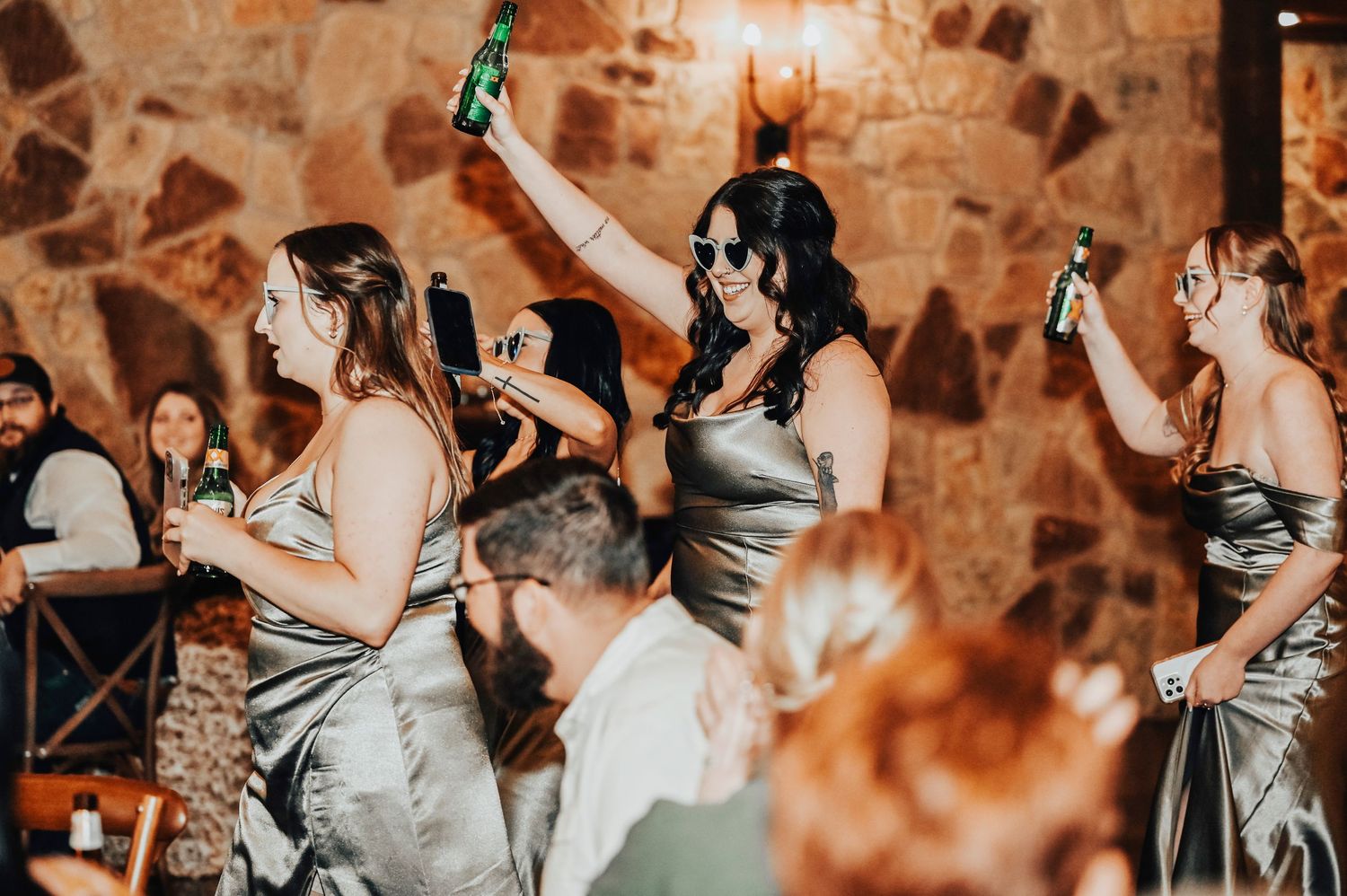 bridesmaids happily dance into the wedding reception wearing their vintage sunglasses and raising their beers