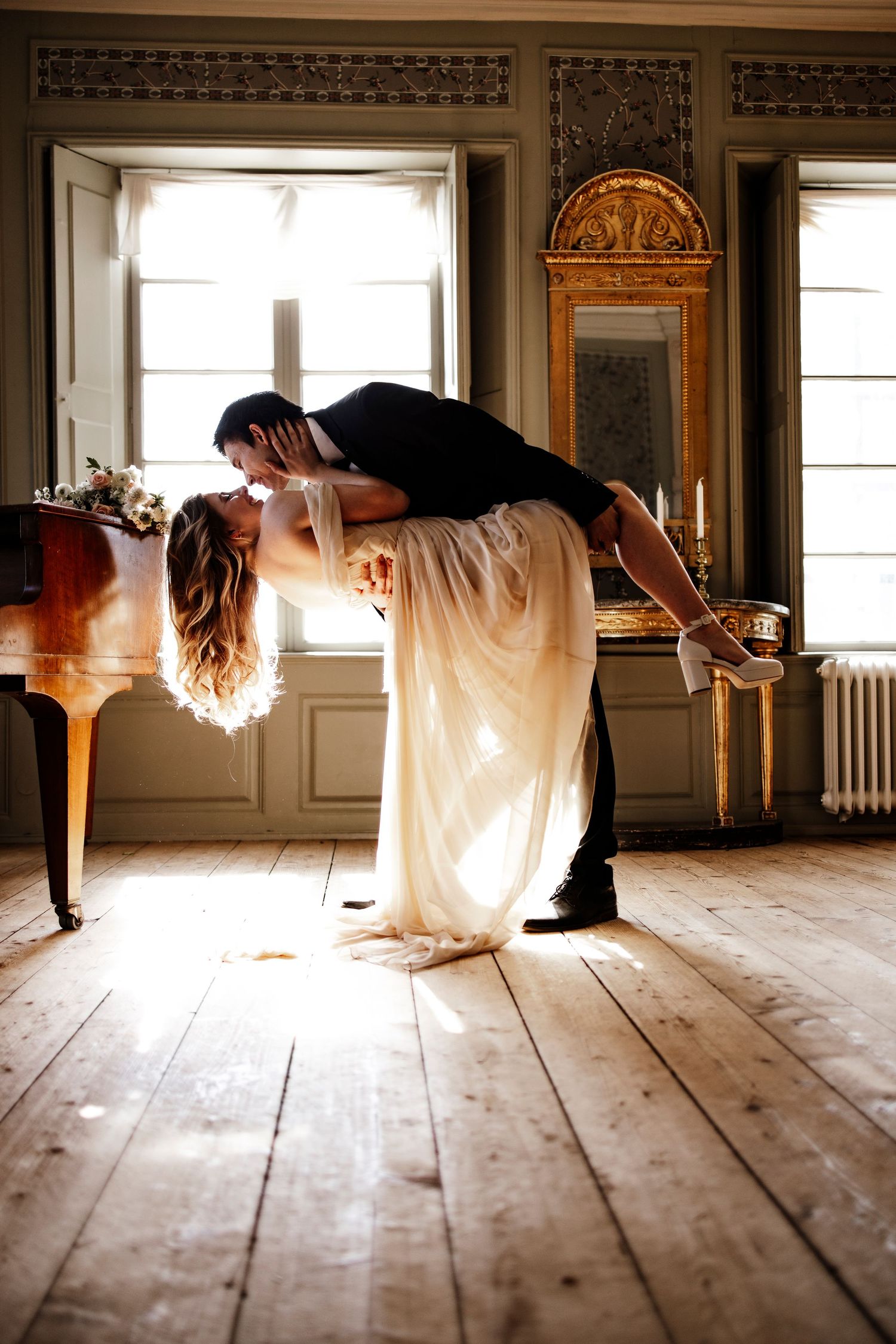 A close-up view of curled brown hair and a white dress with hands clasped gently at the waist in romantic lighting.