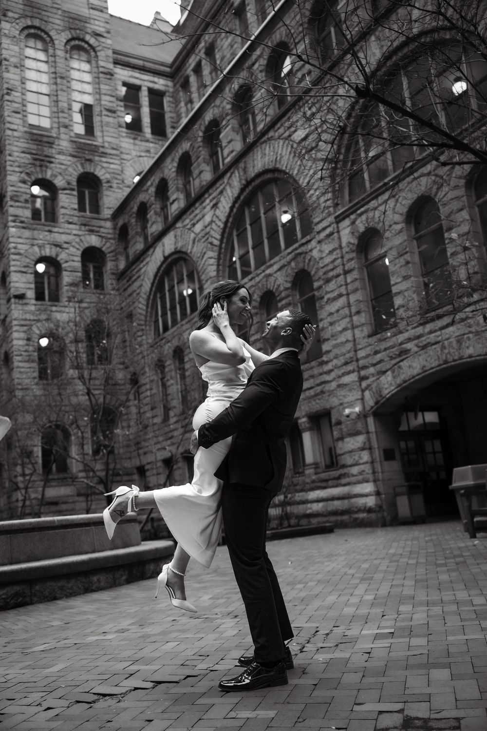 A romantic couple dancing in front of a historic stone building with arched windows and elegant architecture.