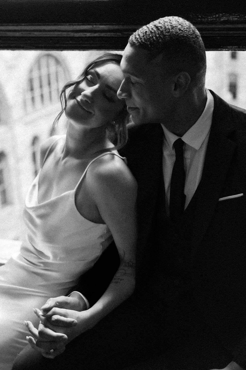 A romantic black and white portrait of a couple on their wedding day, with the bride leaning against her groom's shoulder.