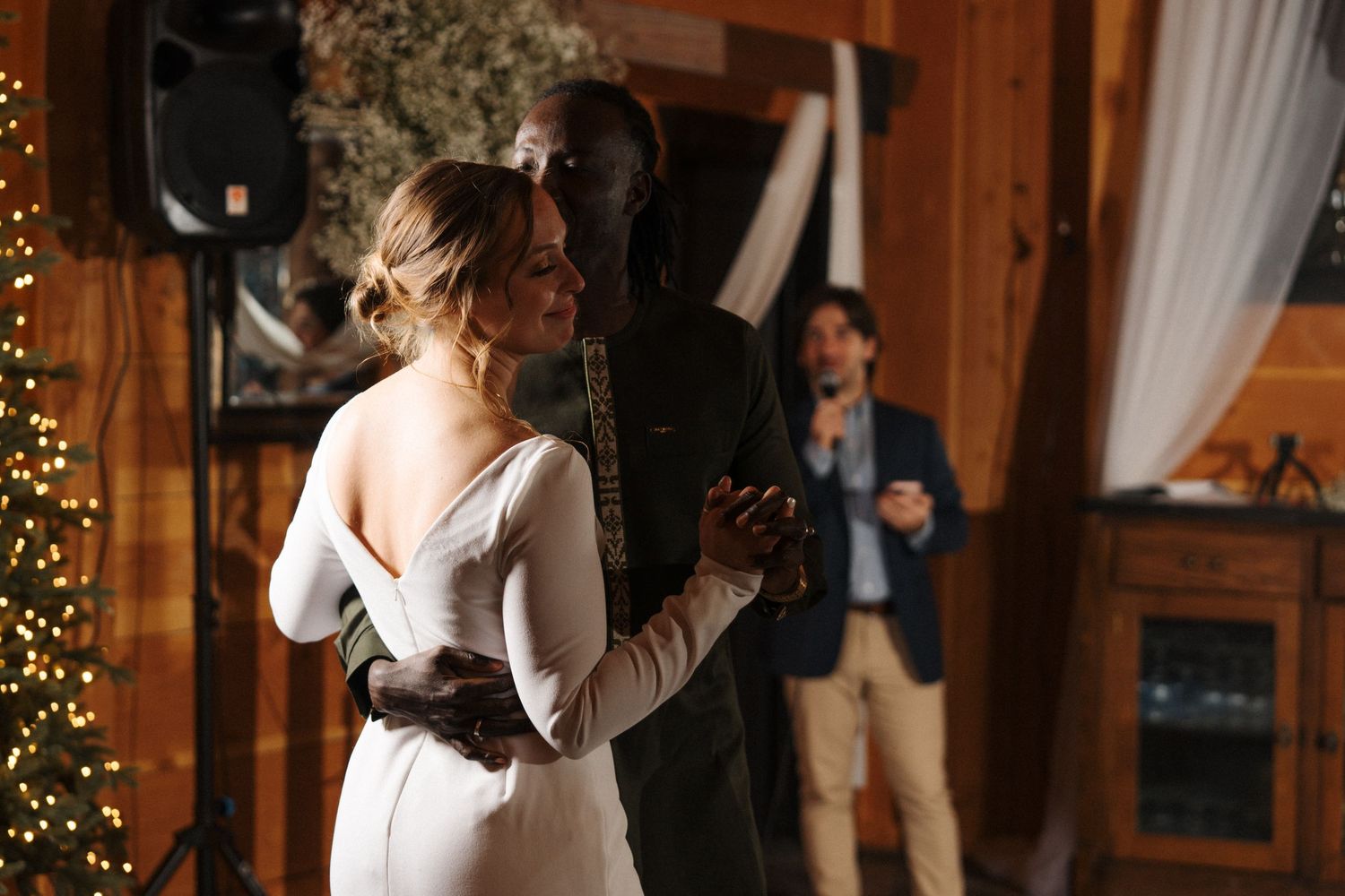 Person in elegant white dress prepares for a celebration in rustic cabin setting with Christmas lights and wood paneling.