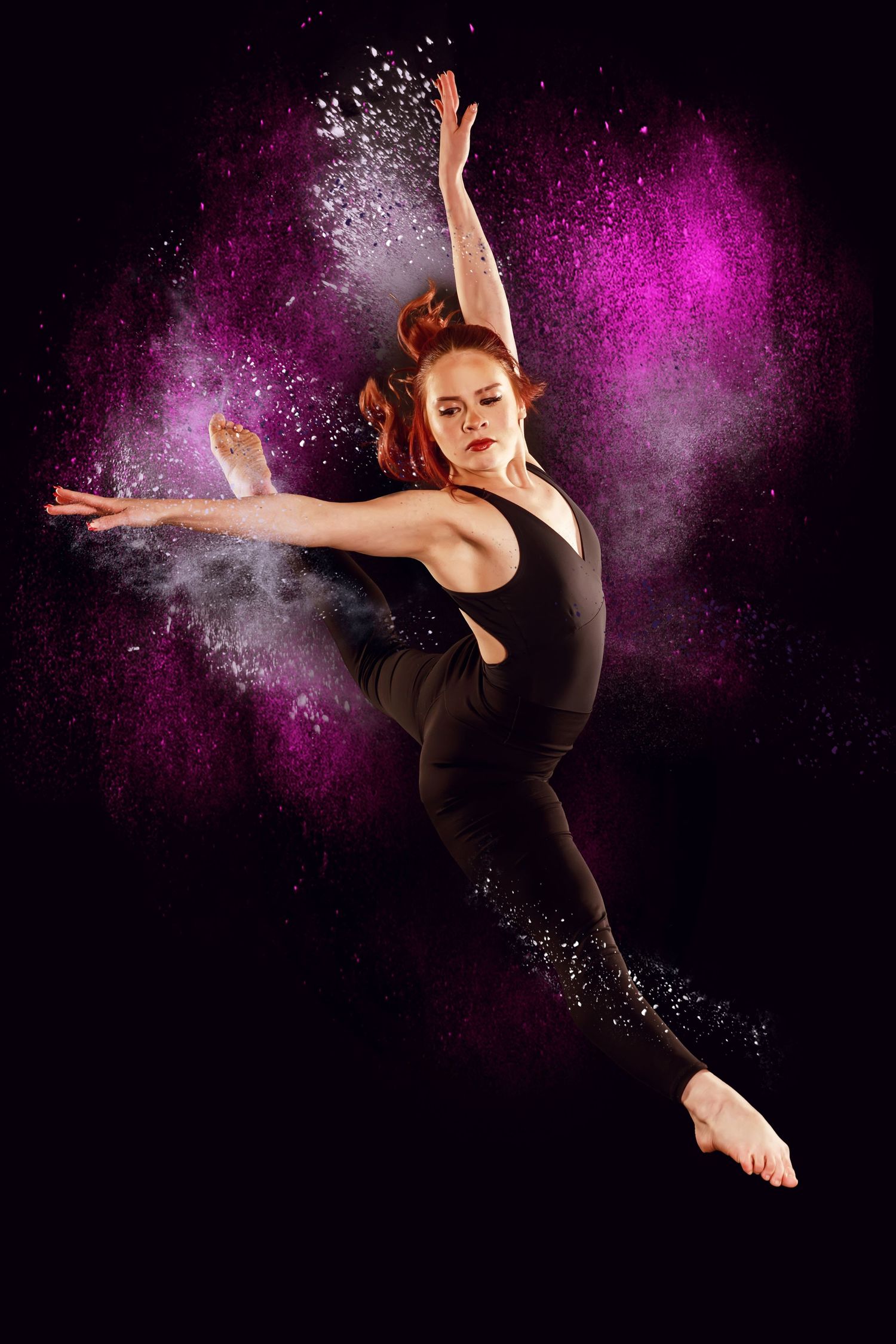 Dancer in black leaping through purple powder effect against dark background.