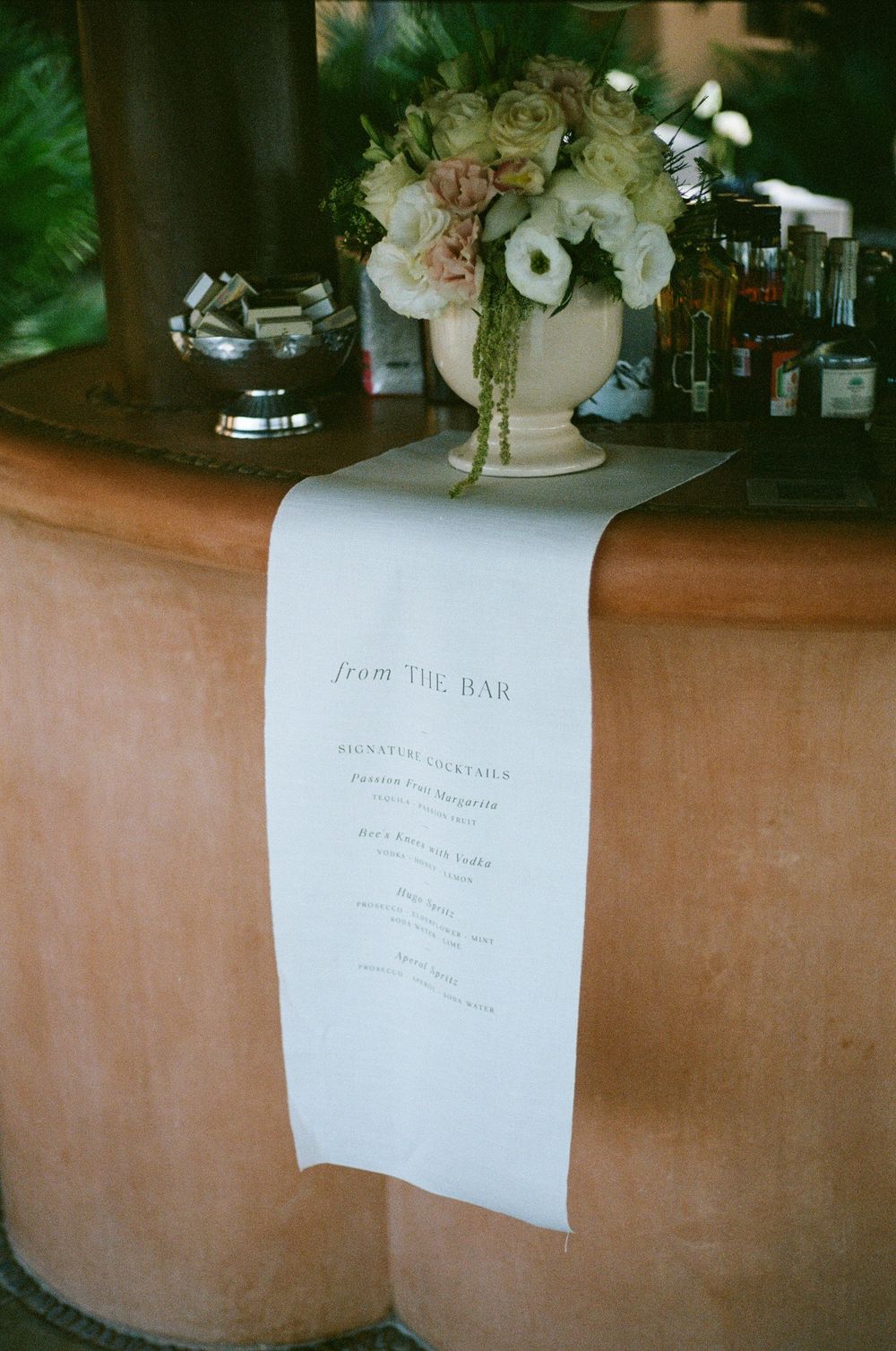 Wedding bar menu displayed on white paper with floral arrangement in cream vase.