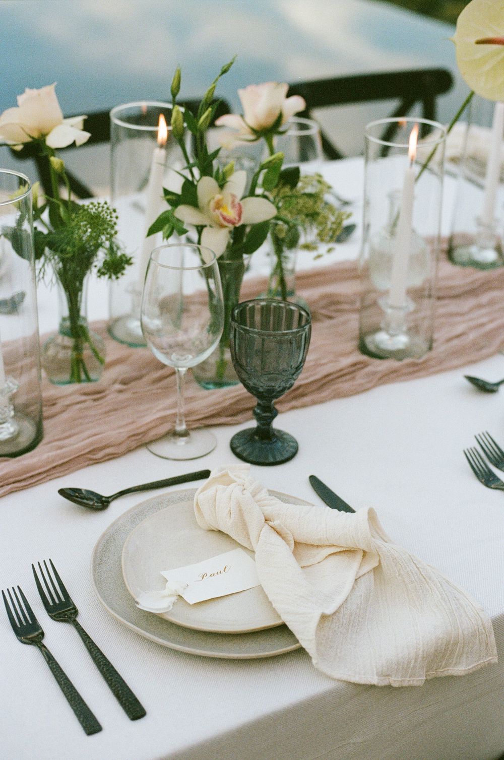 Minimalist place setting with cream napkin, white plates and simple floral centerpieces.