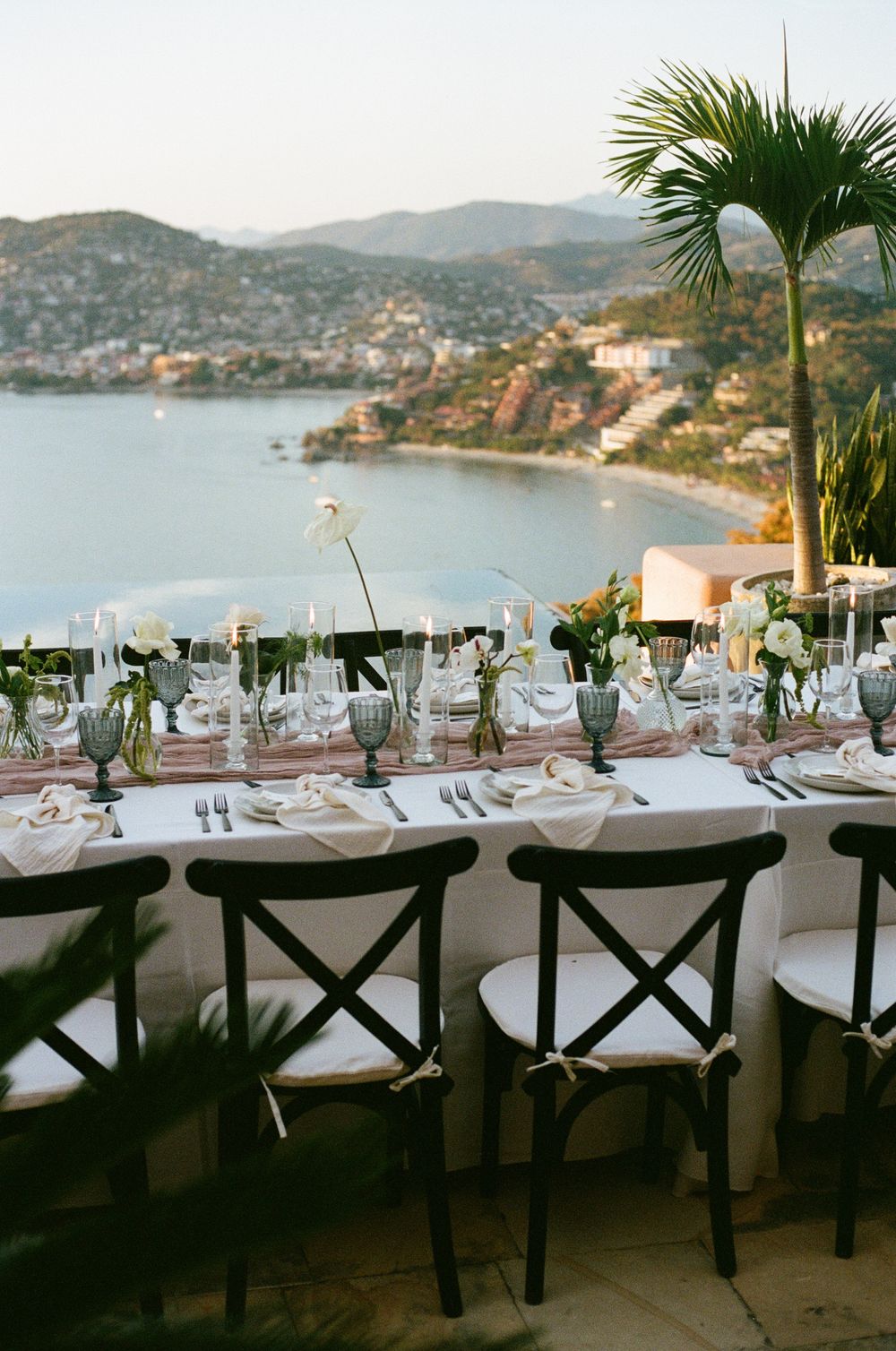 Elegant oceanside dining setup with crossback chairs and coastal mountain views.