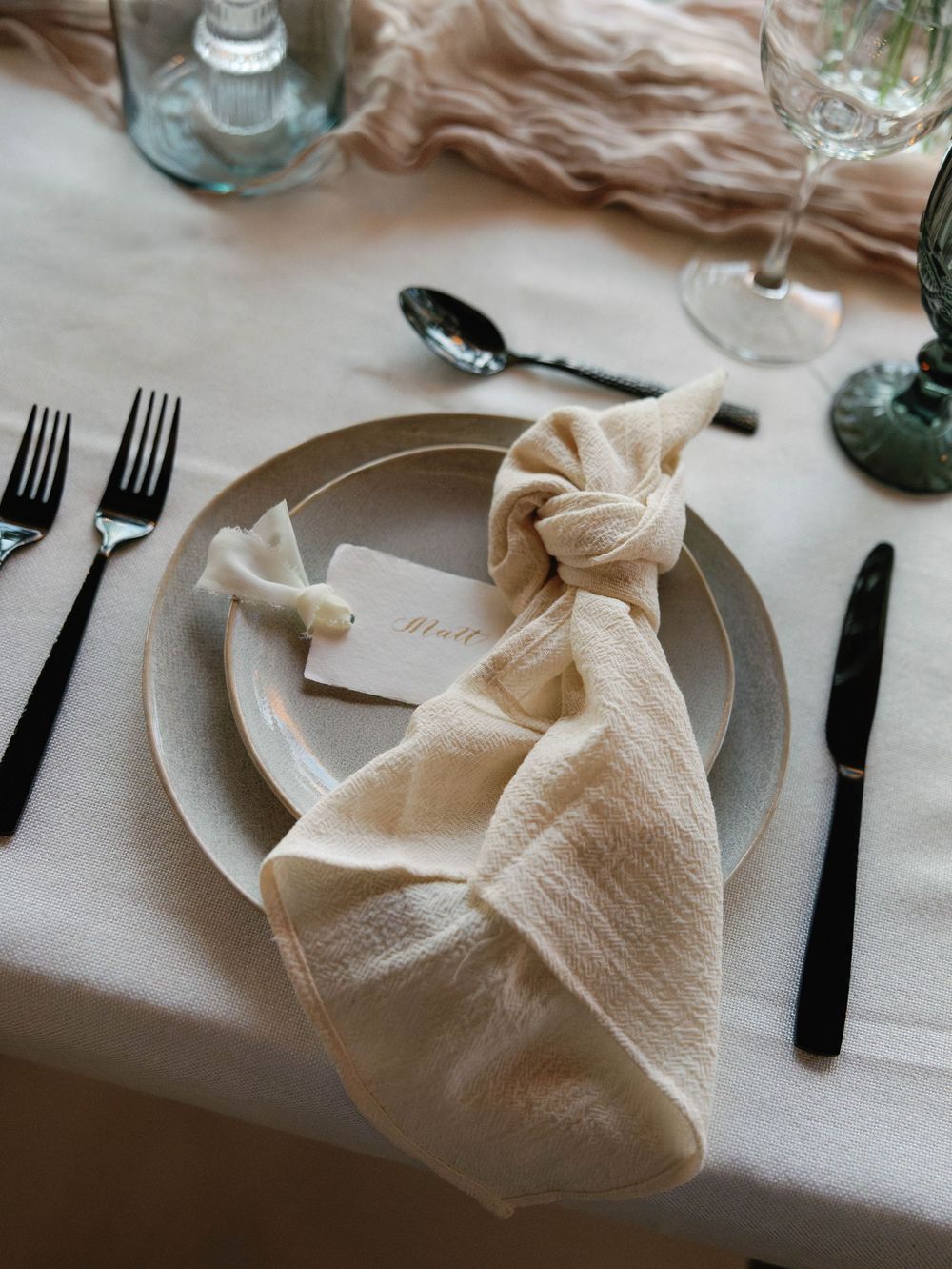 Elegant place setting with cream napkin fold and black cutlery on white tablecloth.