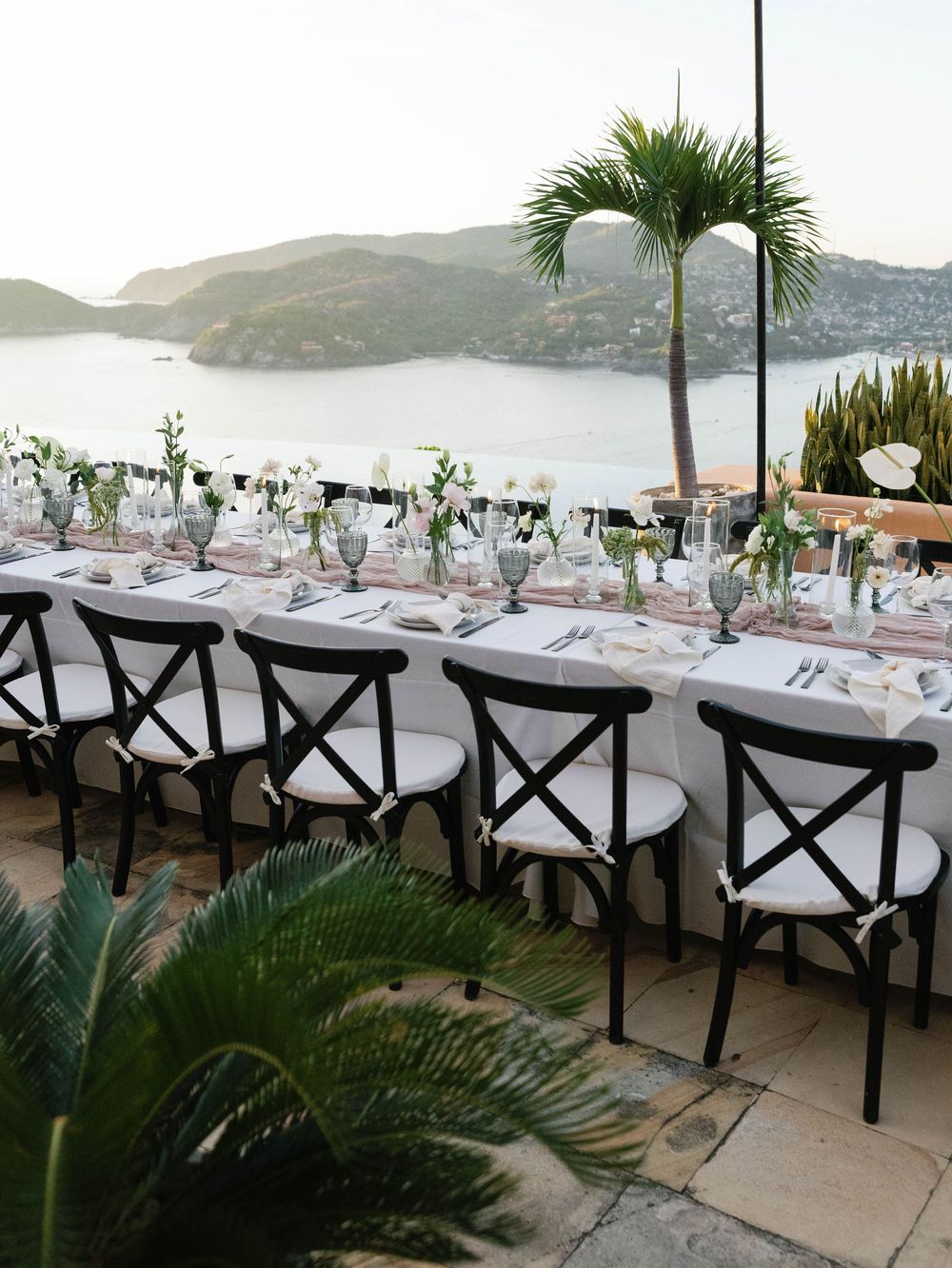 Stunning seaside wedding reception setup with cross-back chairs and mountain views.