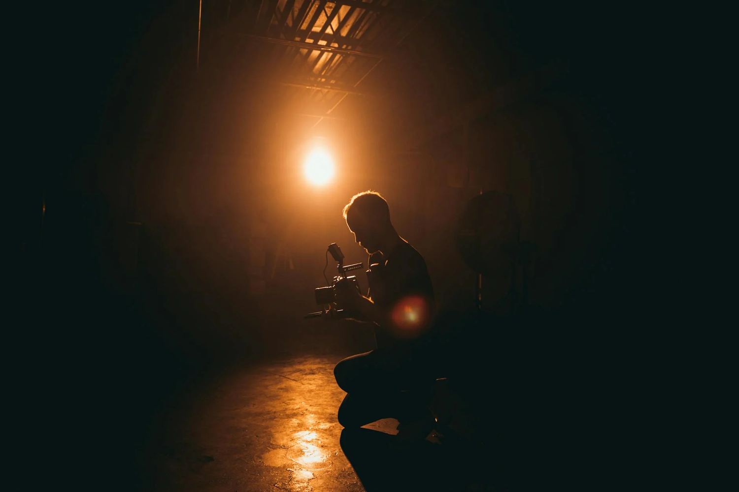 A silhouetted figure crouches on a dark floor while a bright light source creates a dramatic glow from above.