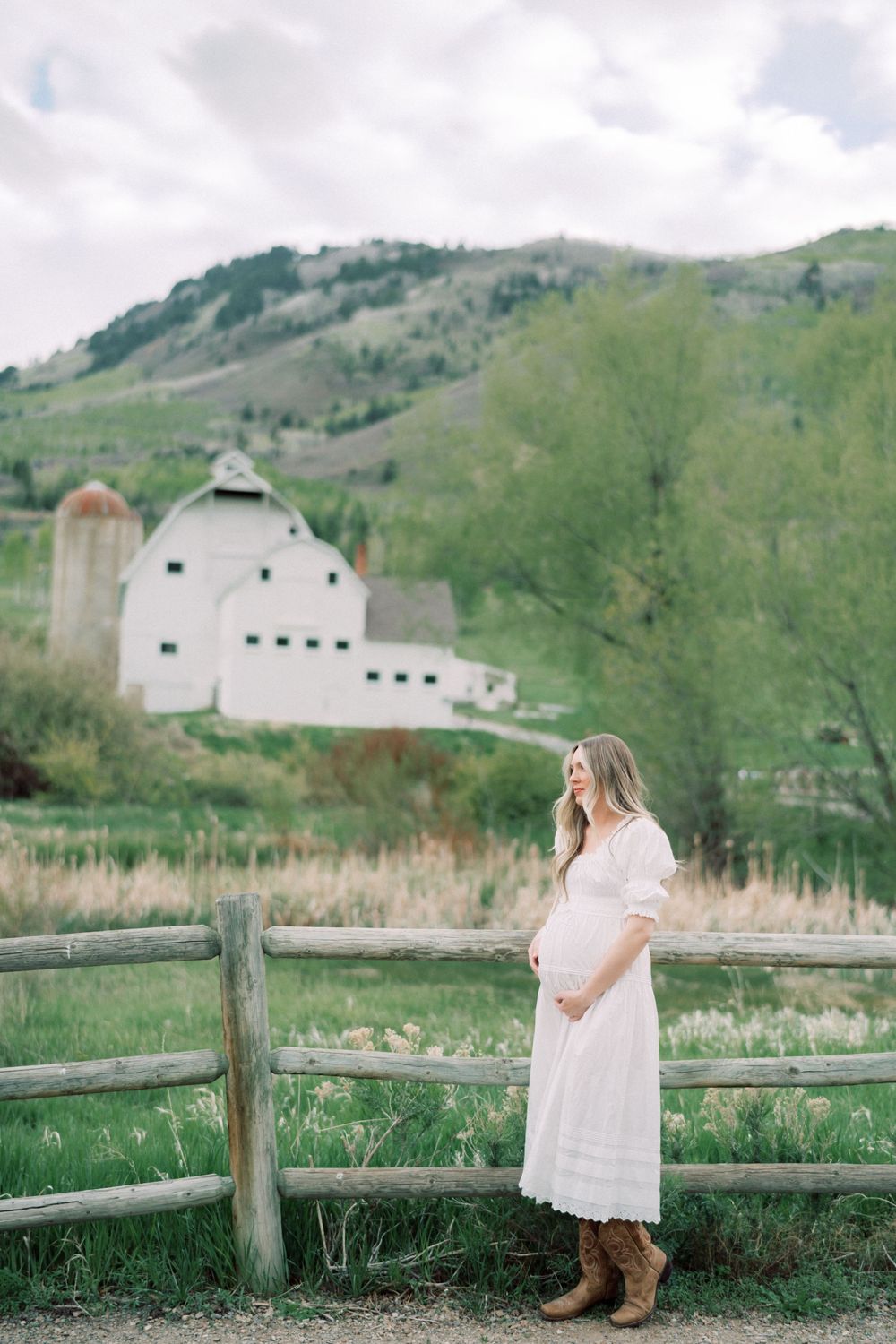 White barn and silo nestled in rolling green hills with rustic wooden fence in the foreground.