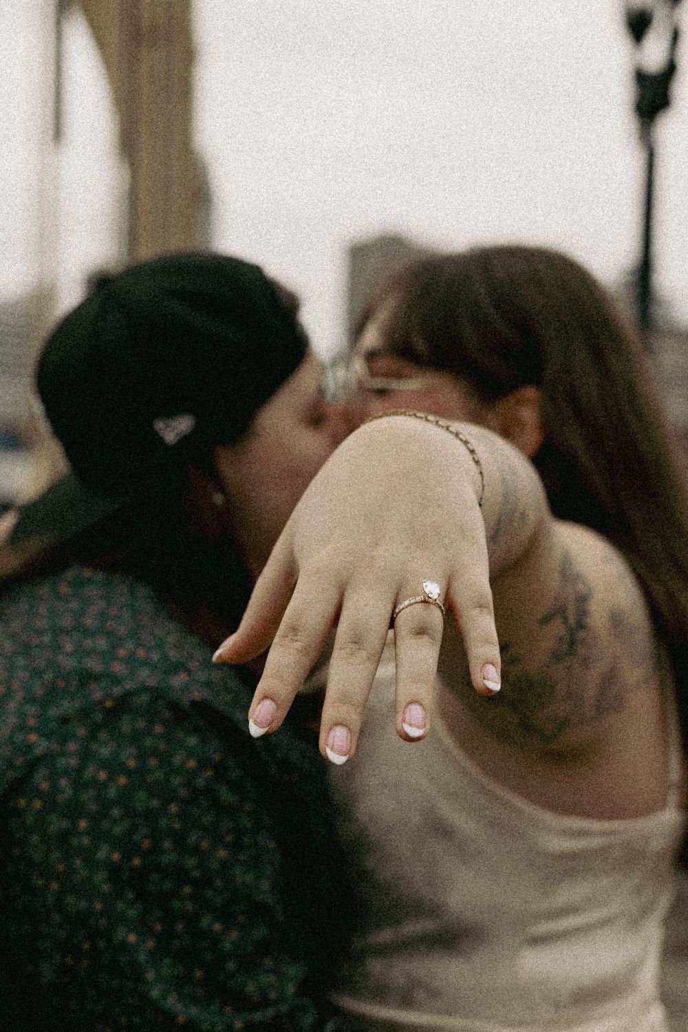 Close up of an engagement ring being shown on person's hand wearing beige sleeve with tattoos visible in background.
