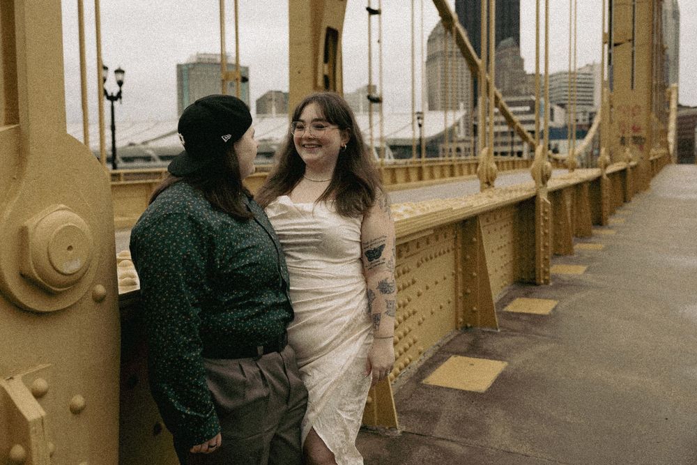 Two people in stylish outfits having a joyful moment on a vintage gold-colored bridge on a cloudy day.