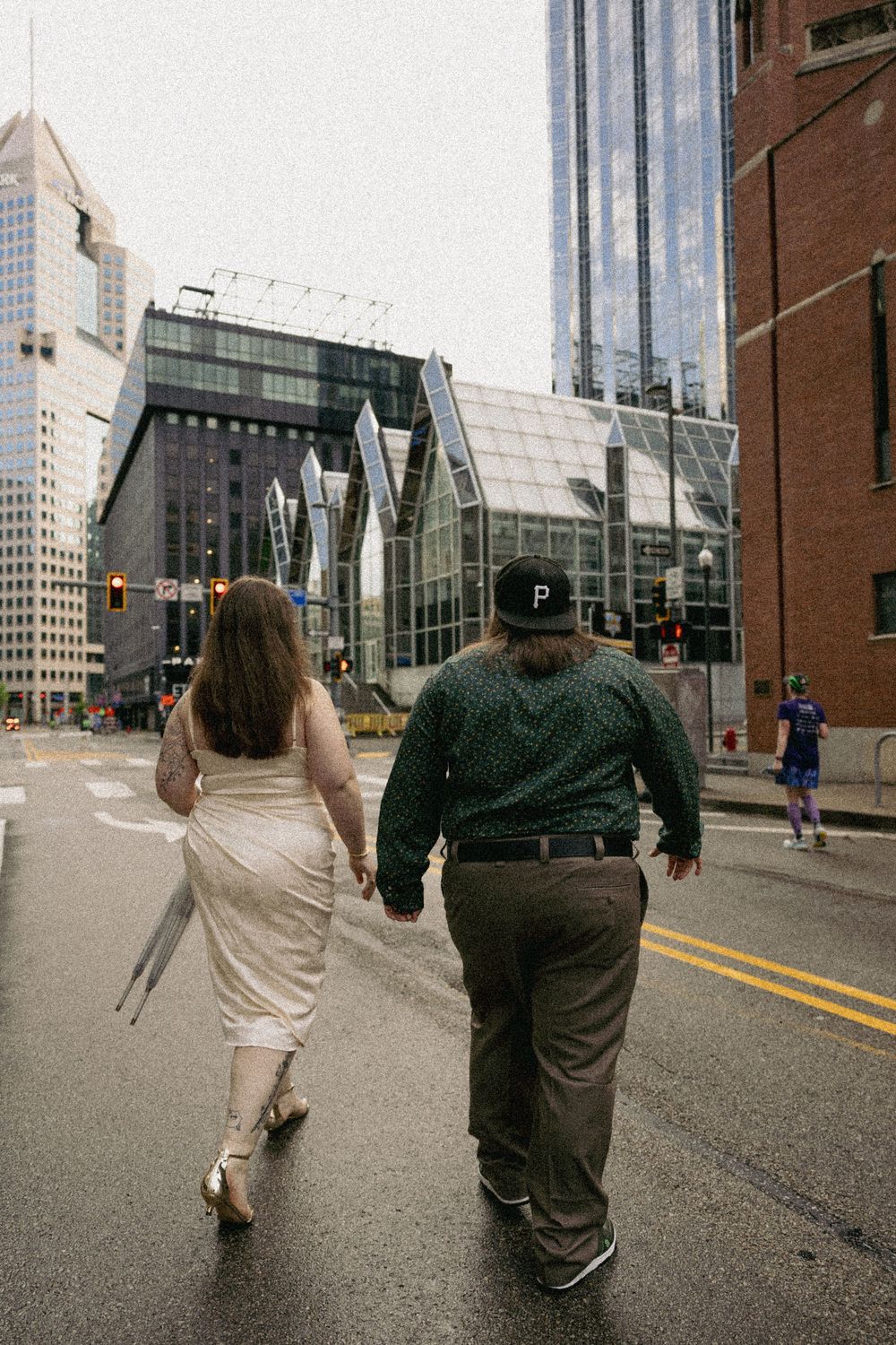 Two people walk down a downtown street with modern glass buildings and skyscrapers towering in the background.