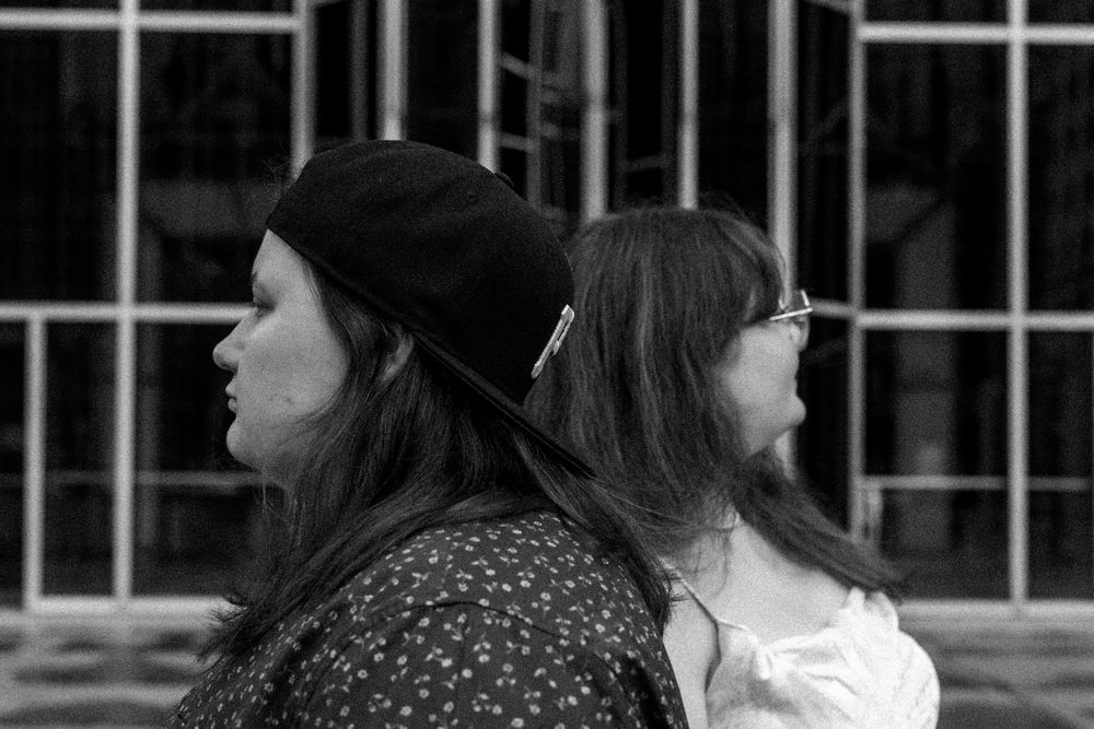 Two figures with long dark hair sit back to back in a black and white photo.