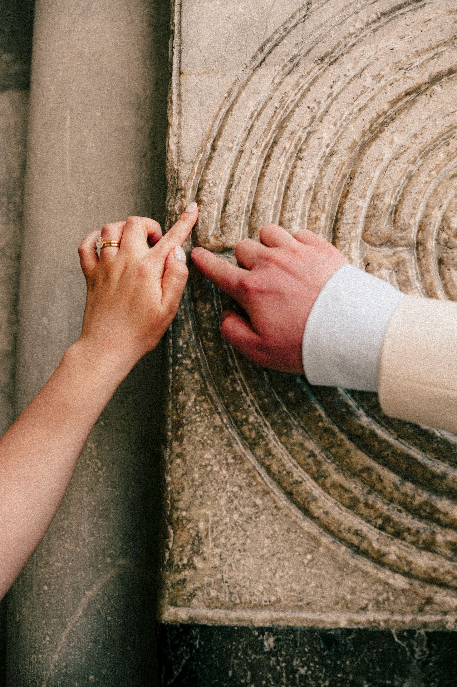 Close-up of hands touching circular pattern carved in stone wall.