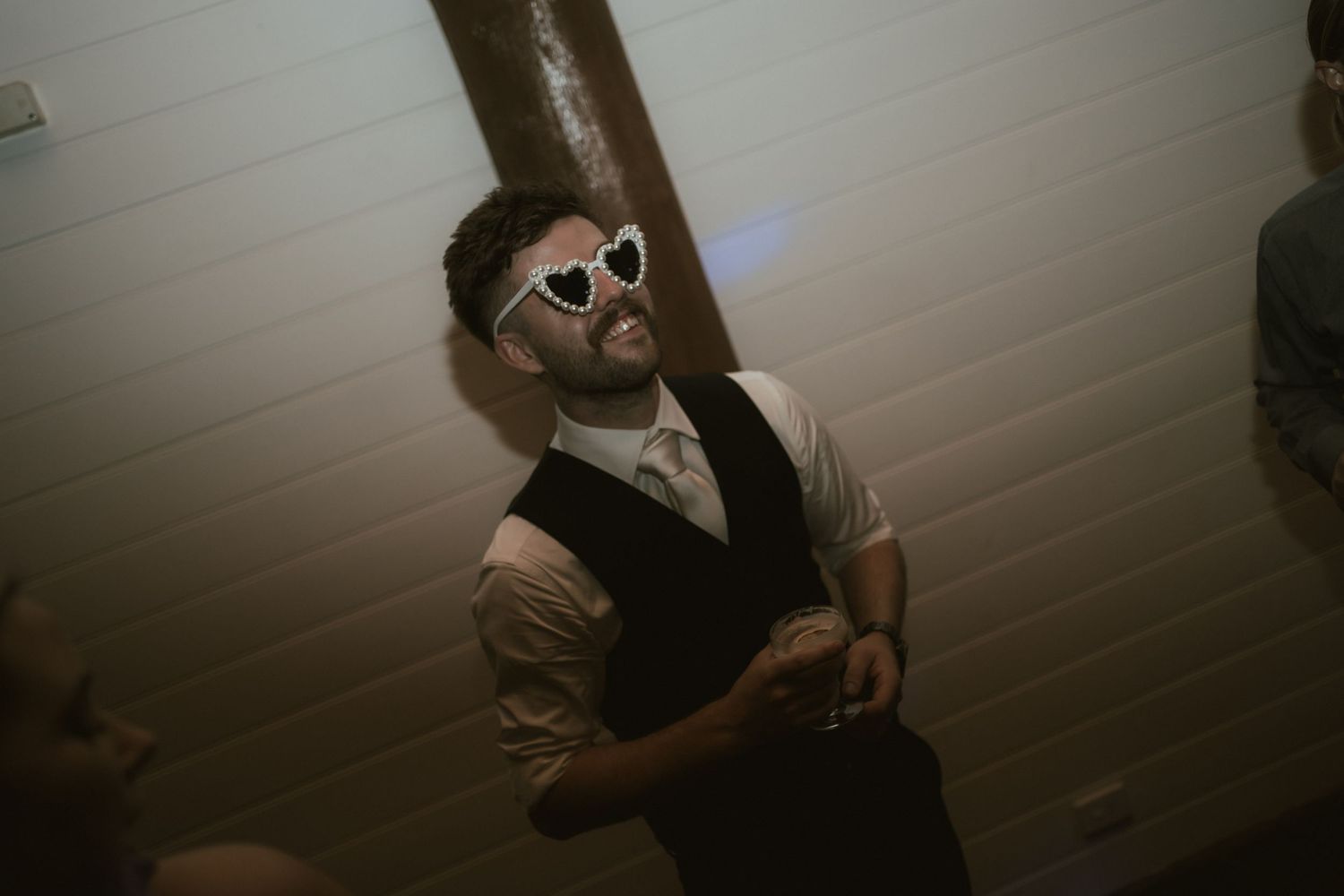 Person in formal vest and white sunglasses dancing at party.