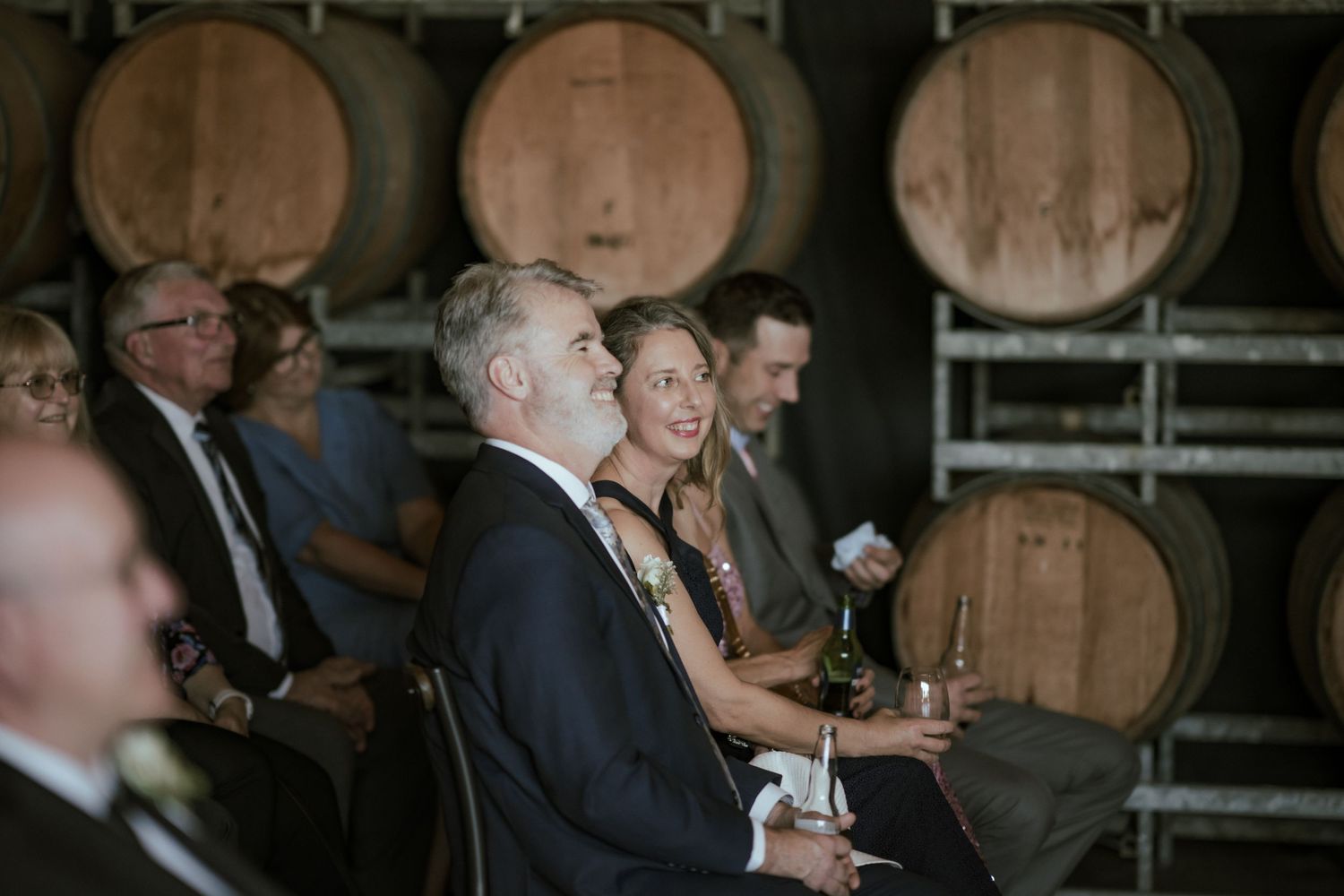 Wedding guests seated in front of wine barrels during ceremony.
